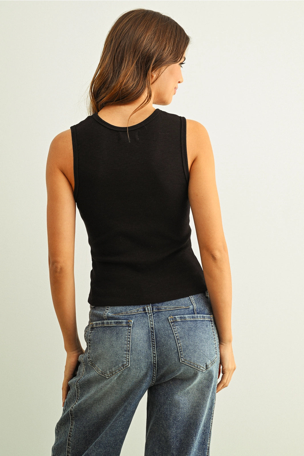 Woman wearing a black sleeveless top and blue jeans on a plain background