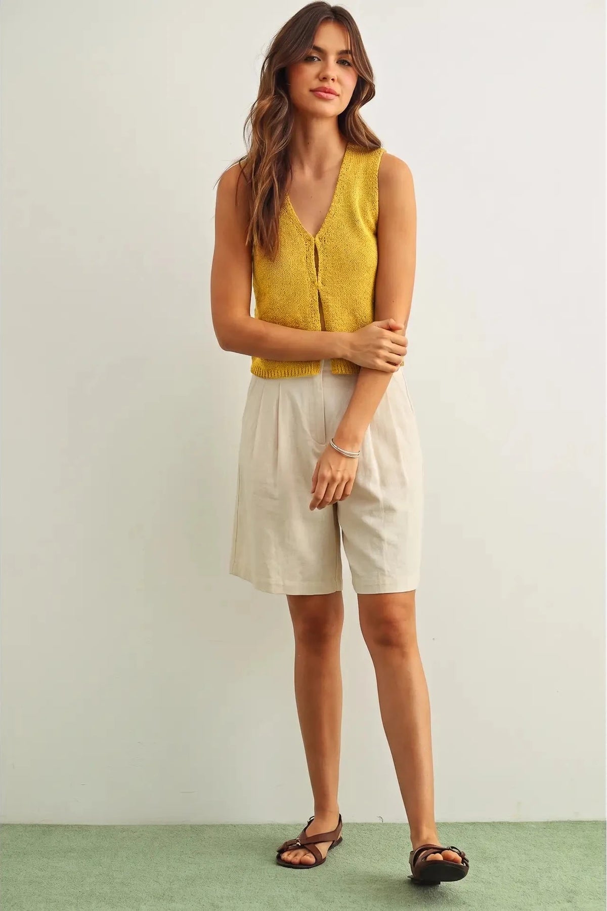 Woman wearing a yellow sleeveless top and beige shorts against a white background