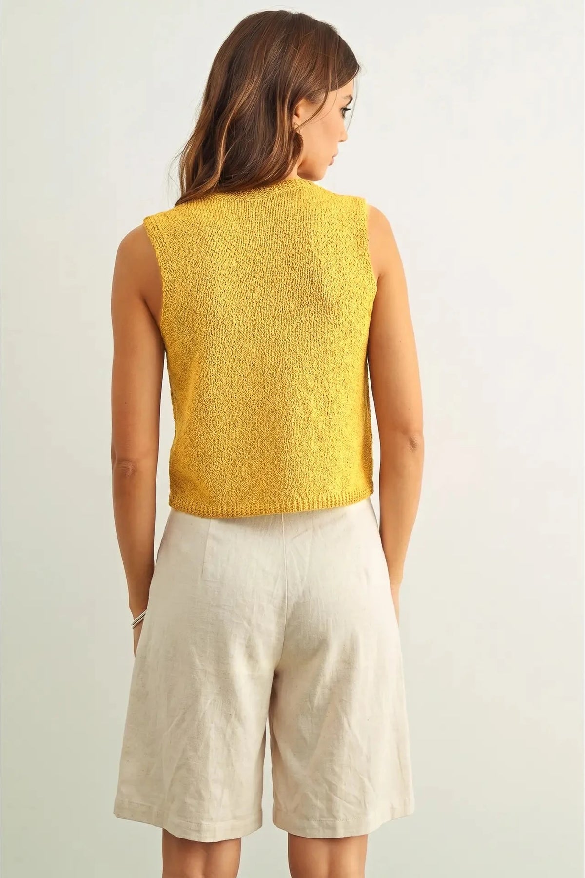 Woman wearing a yellow sleeveless top and beige shorts on a white background