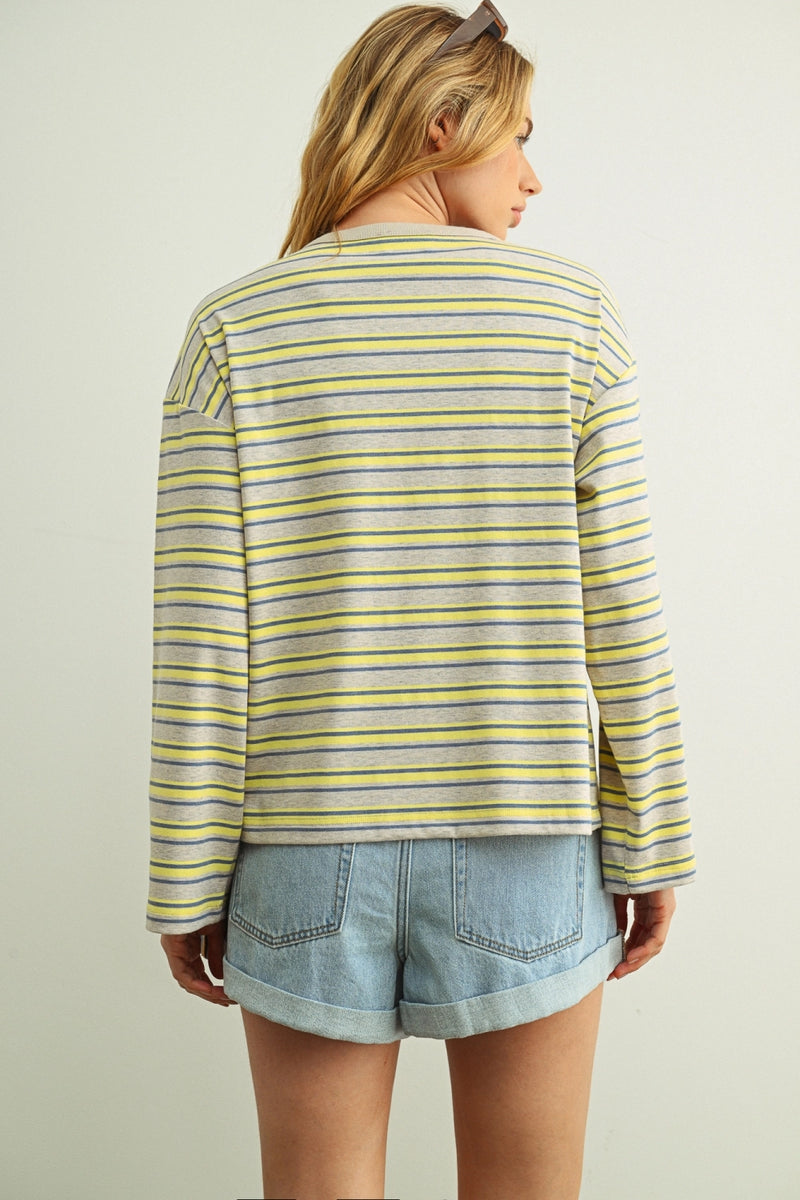 Woman wearing a yellow and gray striped shirt and denim shorts on a plain background