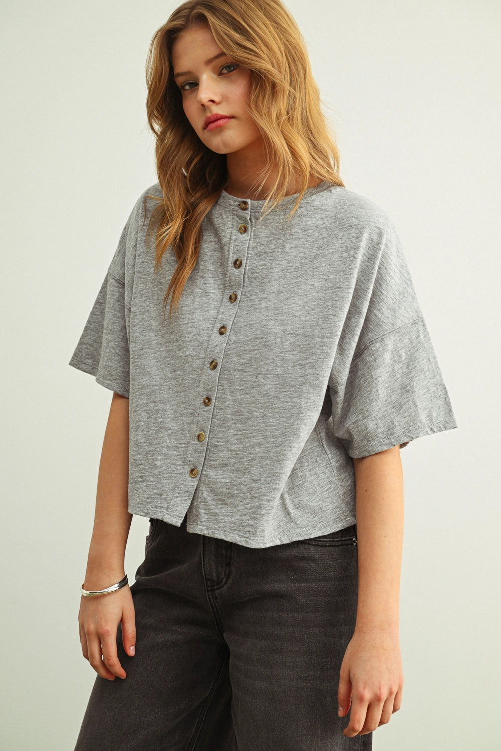 Woman wearing a grey shirt with buttons against a white background.