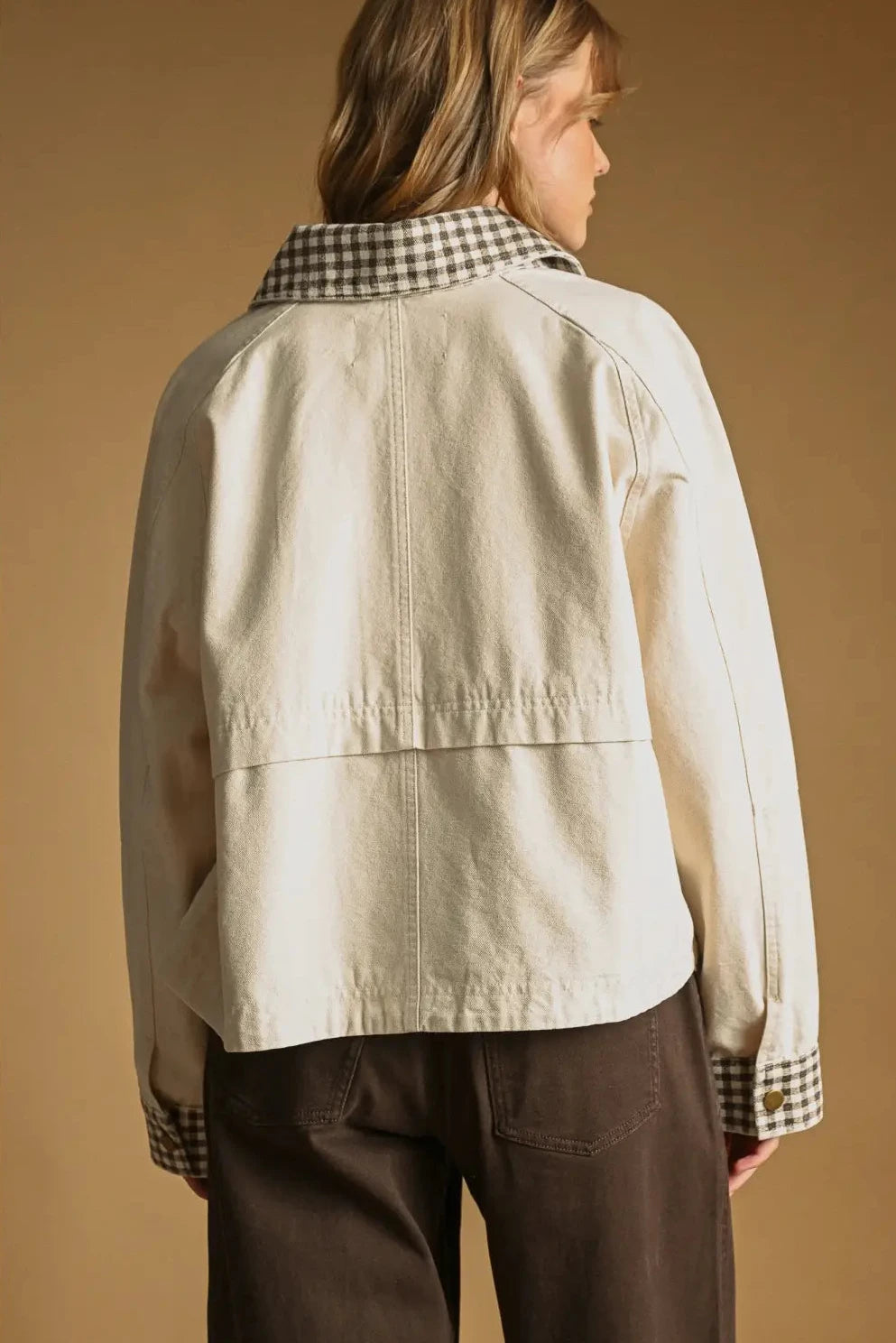 Person wearing a beige jacket with plaid collar against a brown background