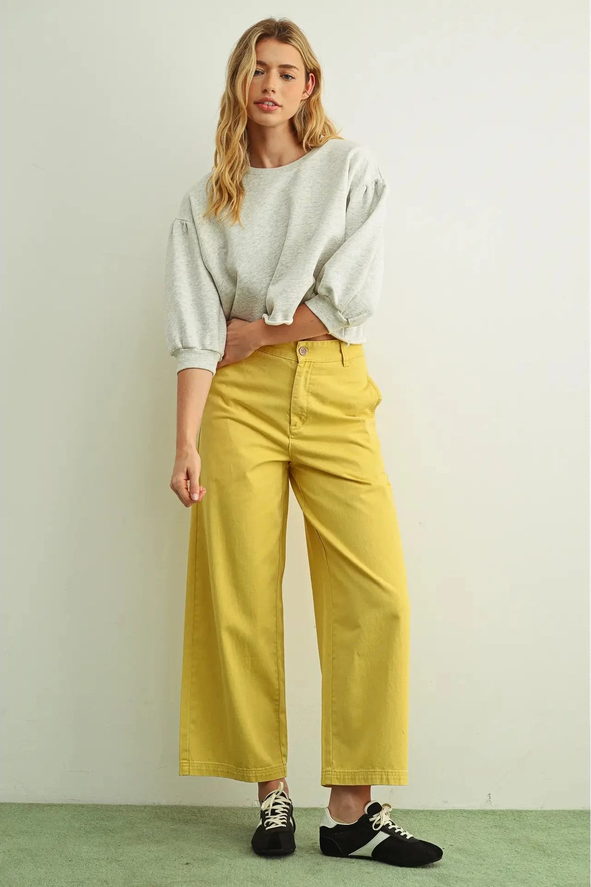 Woman wearing a light gray cropped sweater and yellow pants against a white background