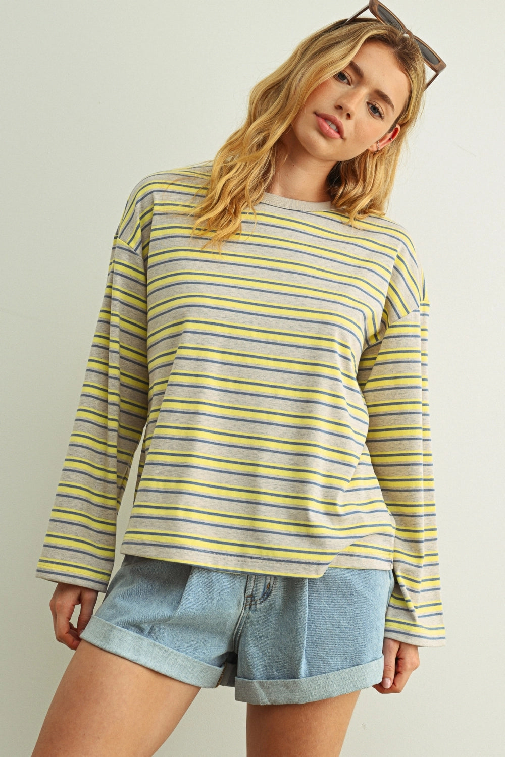 Woman wearing a yellow and gray striped long-sleeve top with denim shorts on a plain background