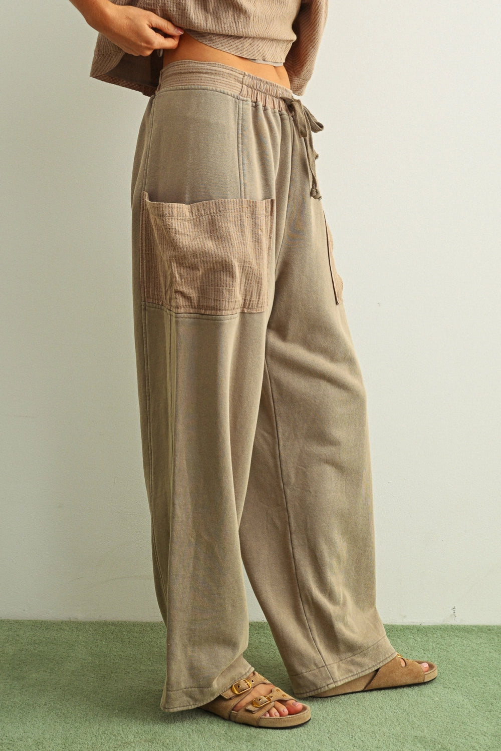 Person wearing beige patchwork pants on a plain background