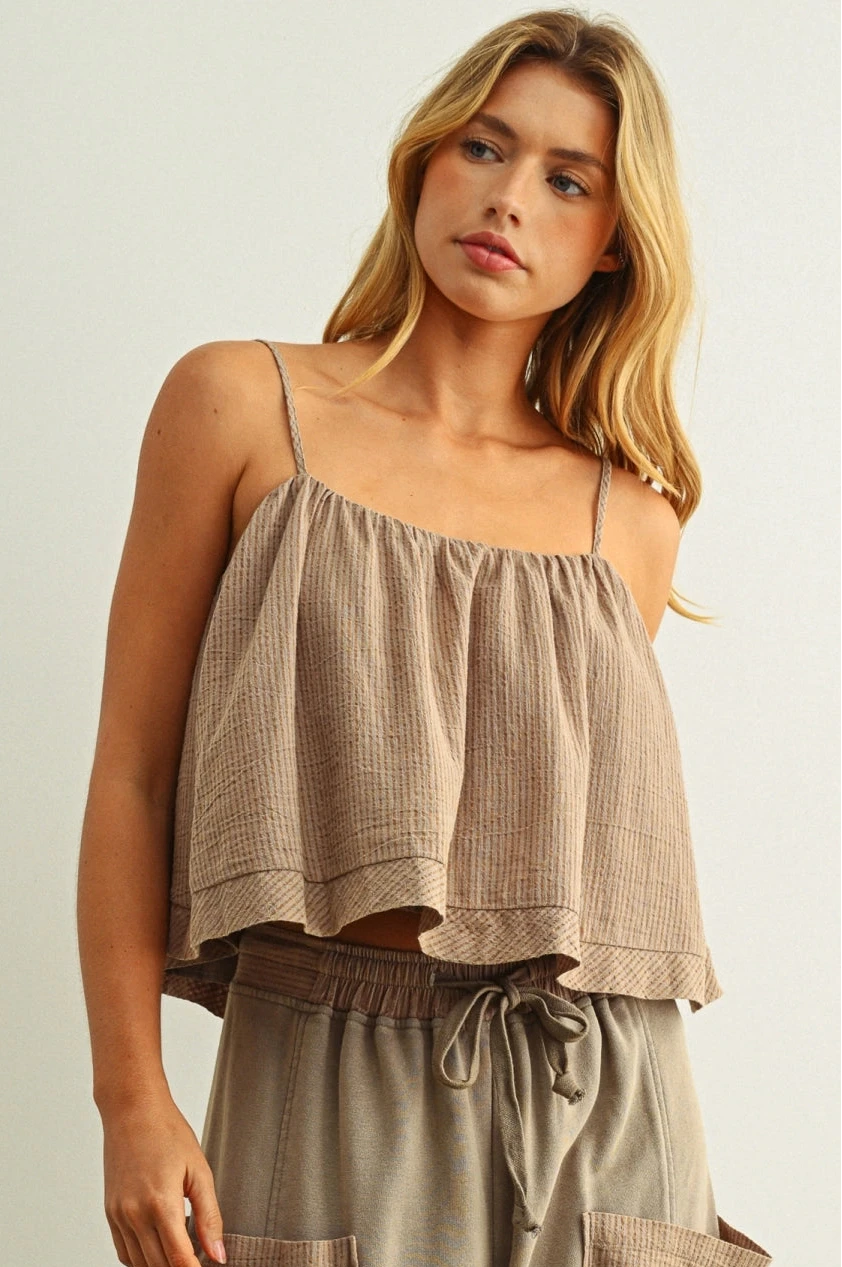 Woman wearing a beige top and brown pants against a plain background