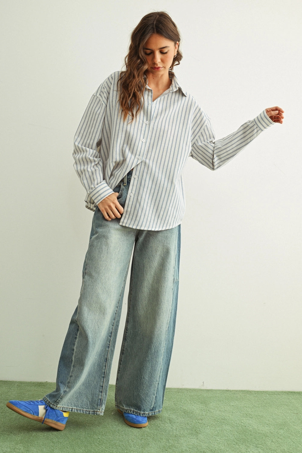 Woman wearing a striped shirt and wide-leg jeans on a green floor with a white wall background