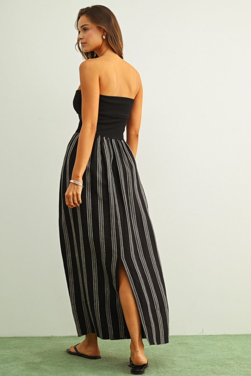 Woman wearing a black strapless dress with white stripes on a plain background