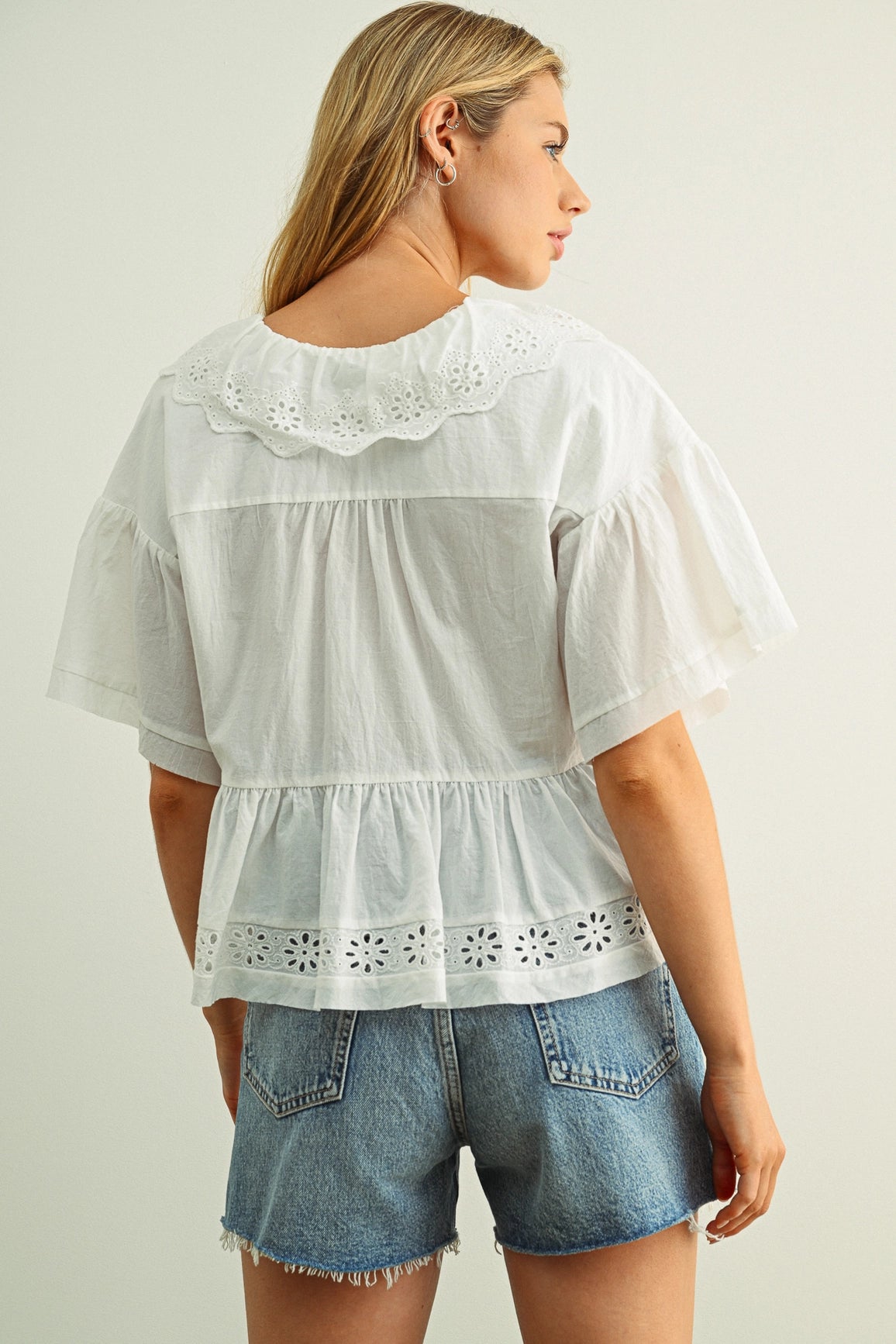 Woman wearing a white blouse with lace details and denim shorts on a plain background
