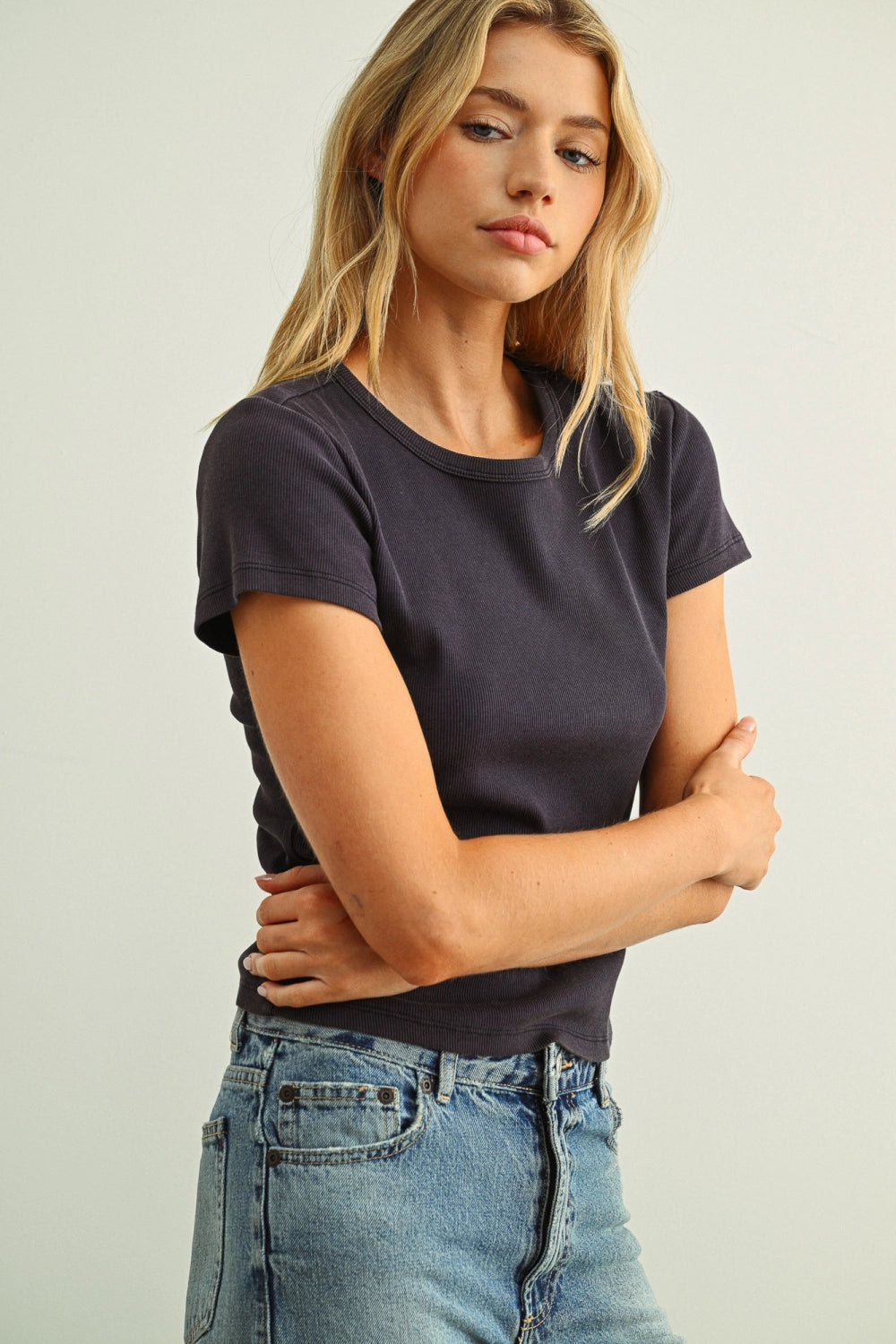 Woman wearing a black t-shirt and blue jeans against a plain background