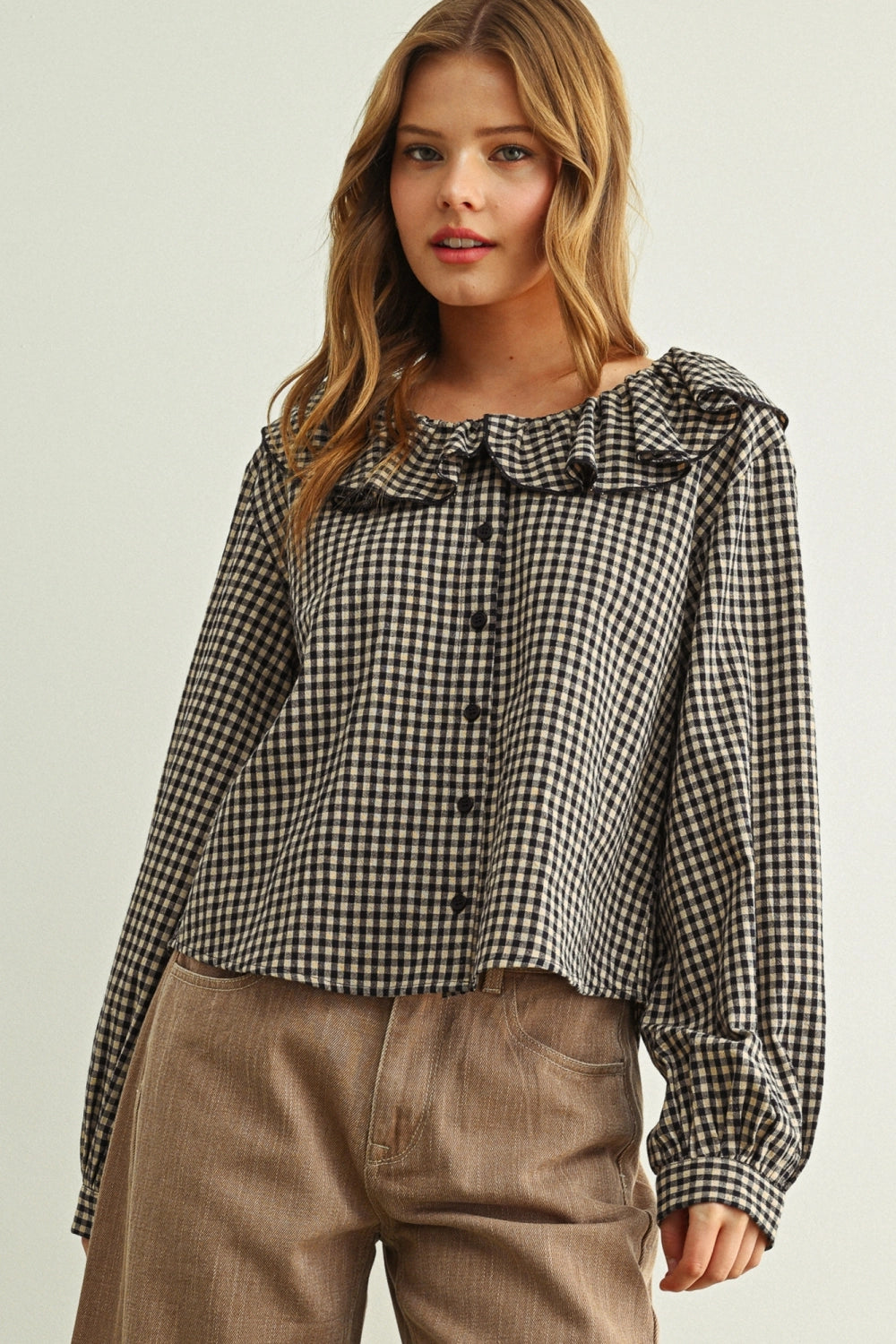 Woman wearing a black and white checkered blouse with ruffled details on a plain background
