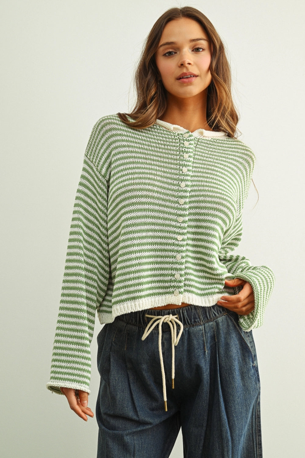 Woman wearing a green striped sweater and blue jeans against a plain background