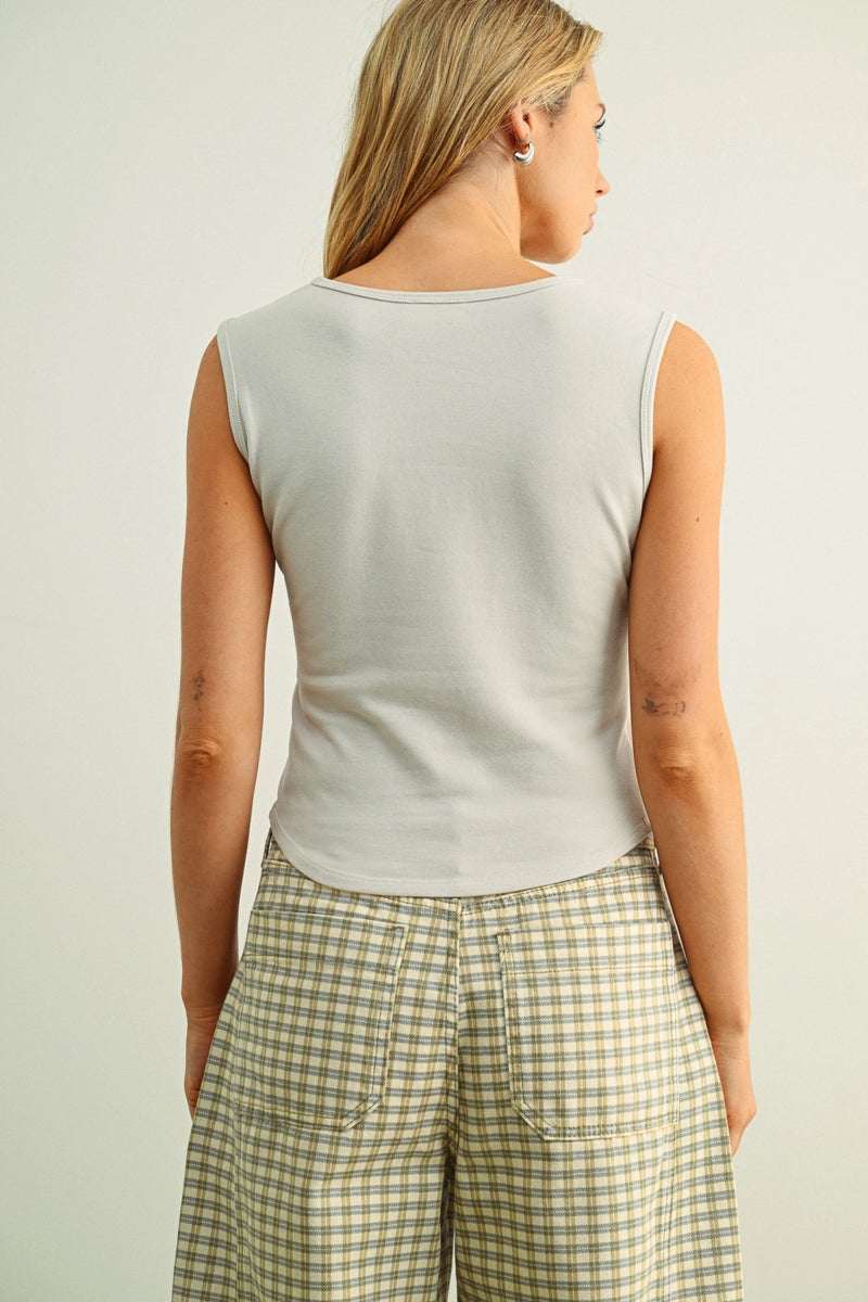 Woman wearing a light gray sleeveless top and plaid pants against a plain background