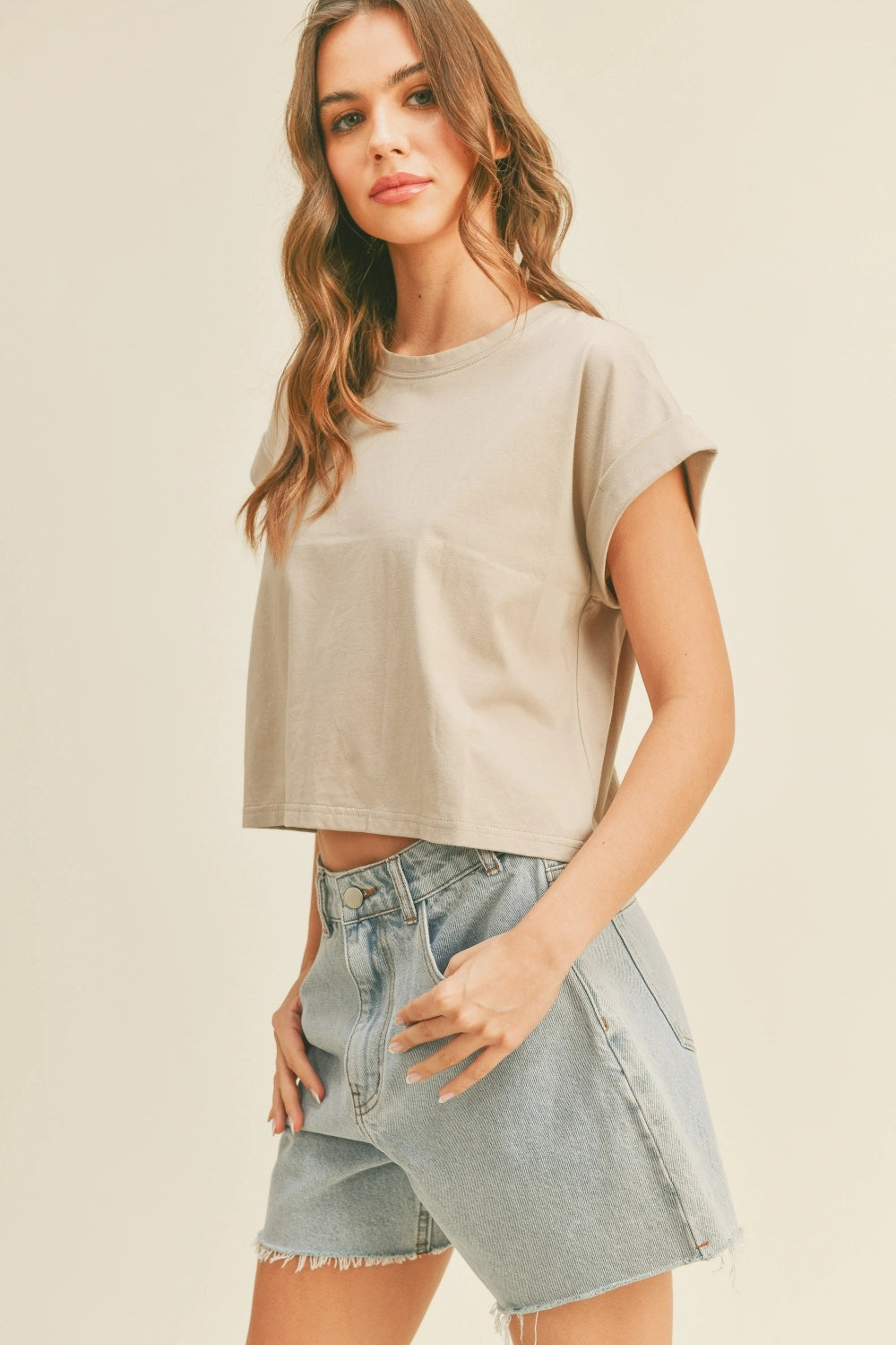Woman wearing a beige crop top and denim shorts on a plain background