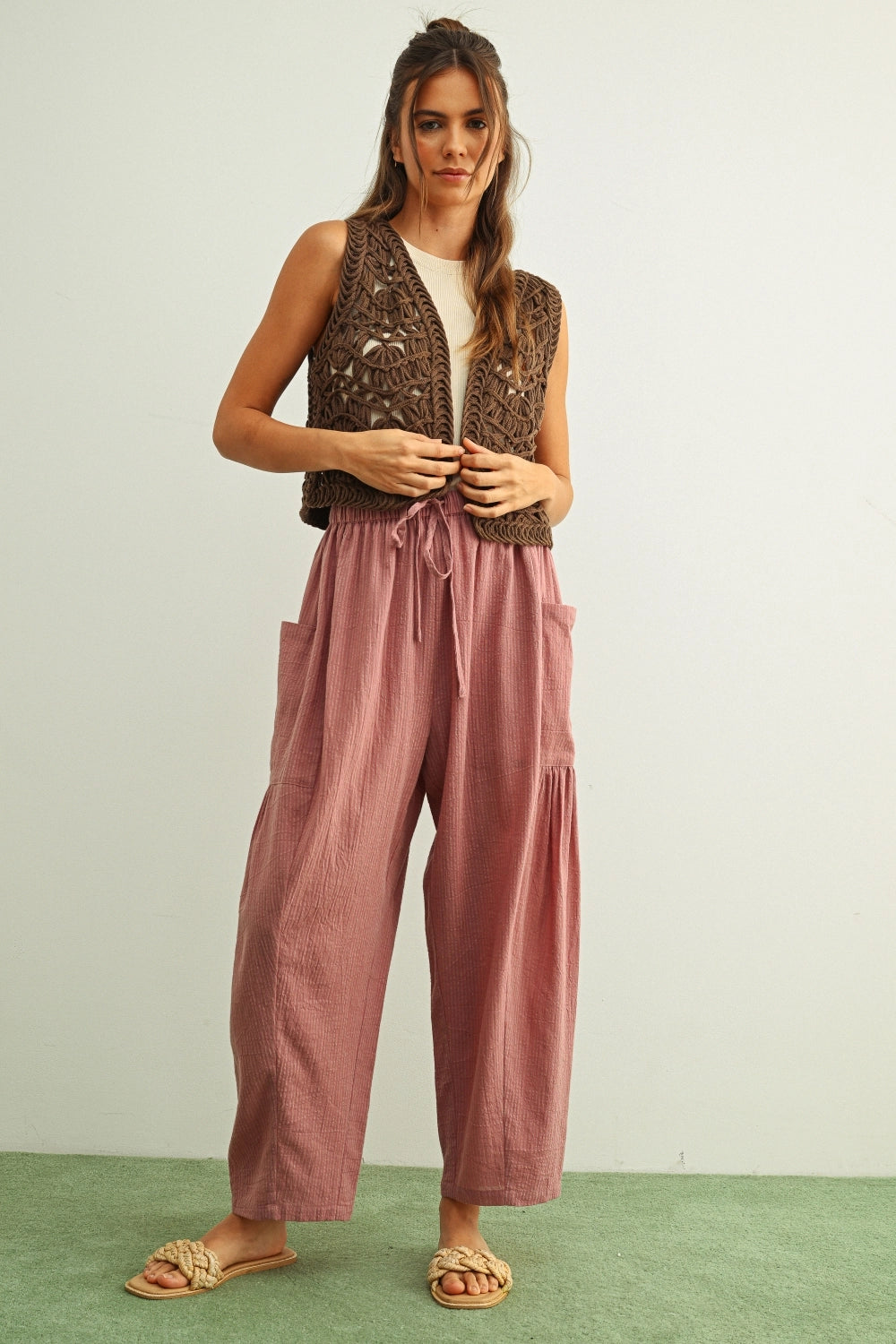 Woman wearing a brown patterned vest and pink pants on a light green background
