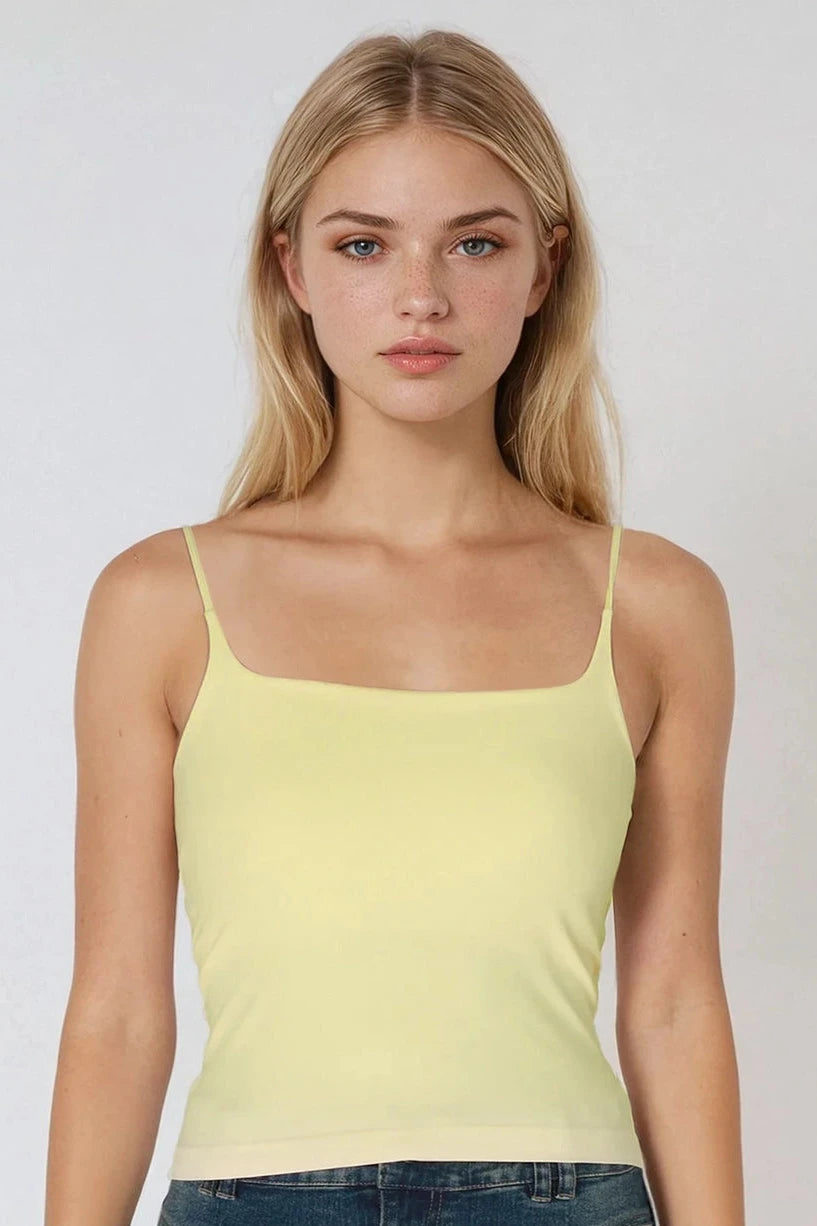 A blonde model wearing a pale yellow spaghetti-strap camisole top and blue jeans, photographed against a plain light gray studio background.