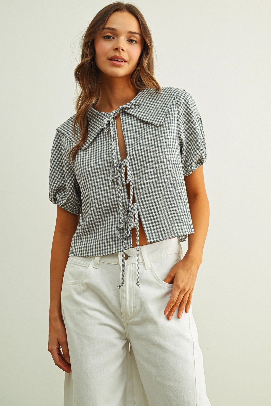 Woman wearing a checkered shirt and white pants against a plain background
