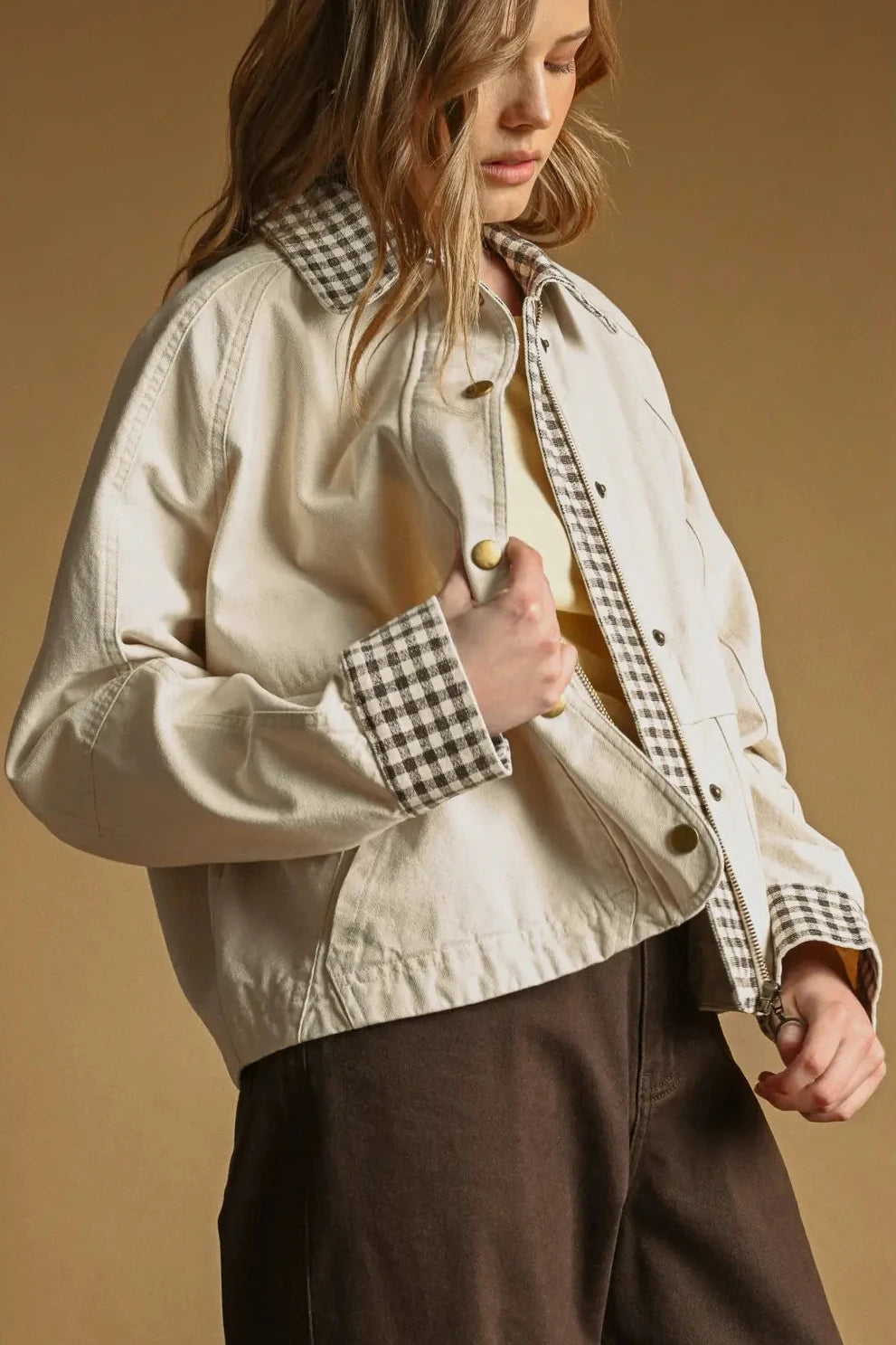 Person wearing a beige jacket with checkered collar and cuffs on a brown background
