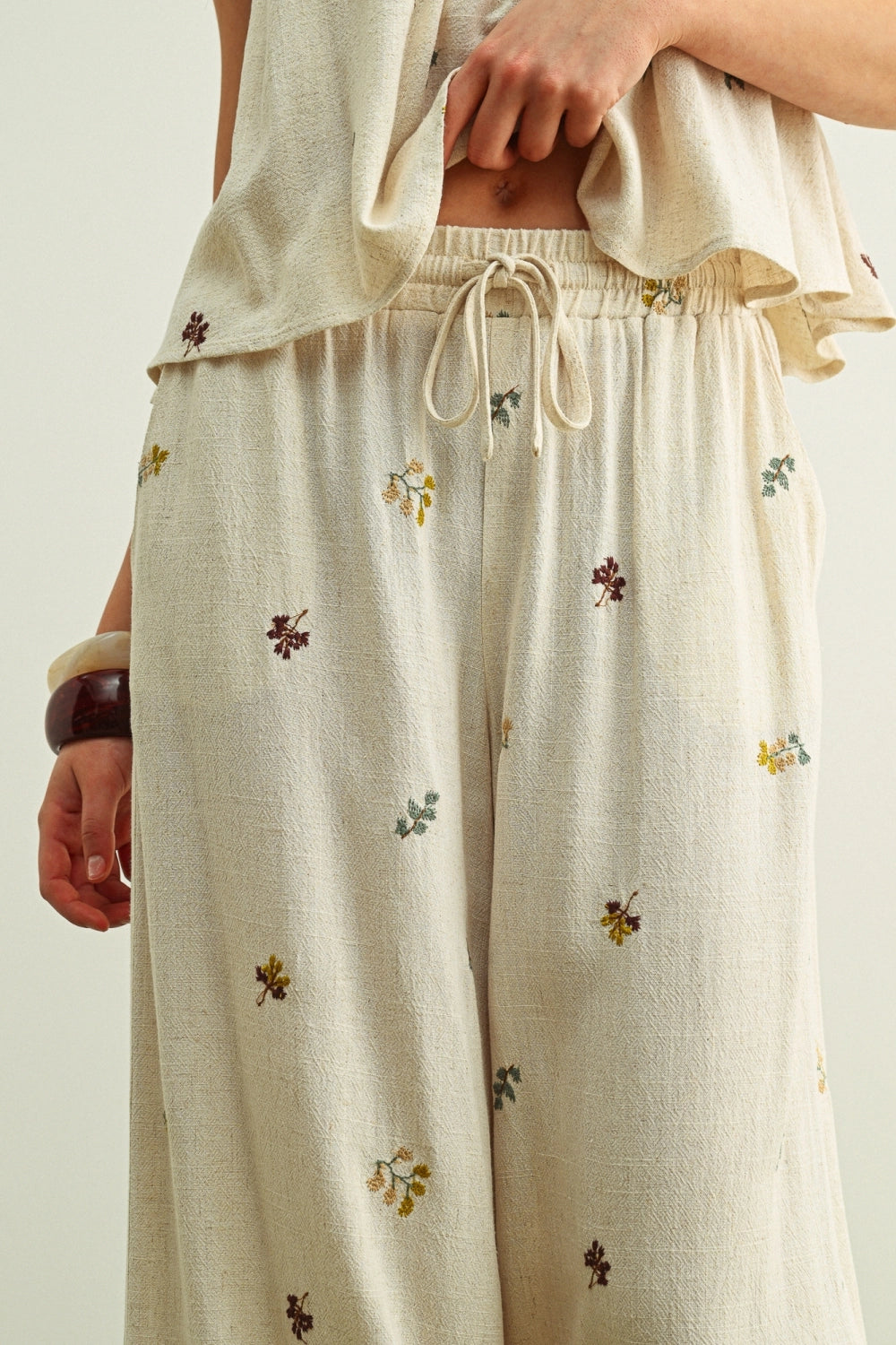 Beige pants with floral embroidery worn by a person on a neutral background