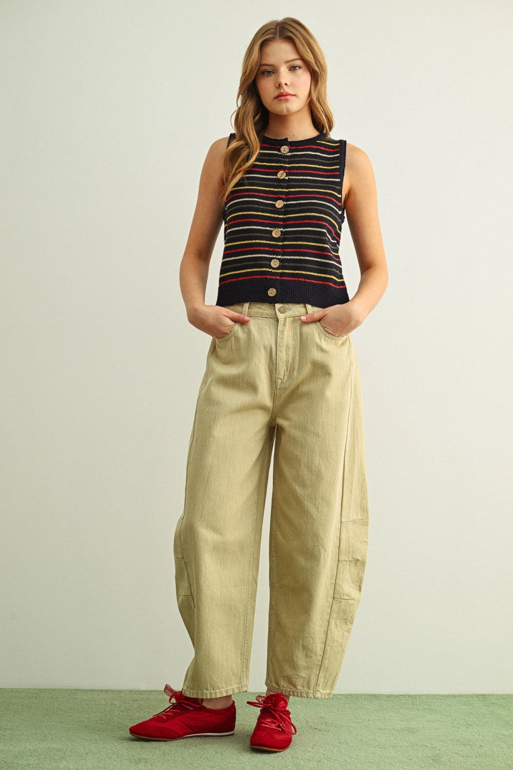 Woman wearing a striped sleeveless top and beige pants with red shoes on a light background