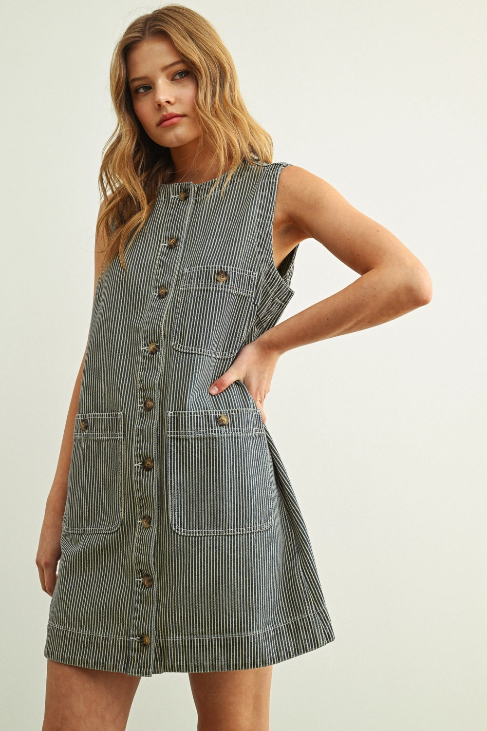 Woman wearing a sleeveless denim dress against a plain background