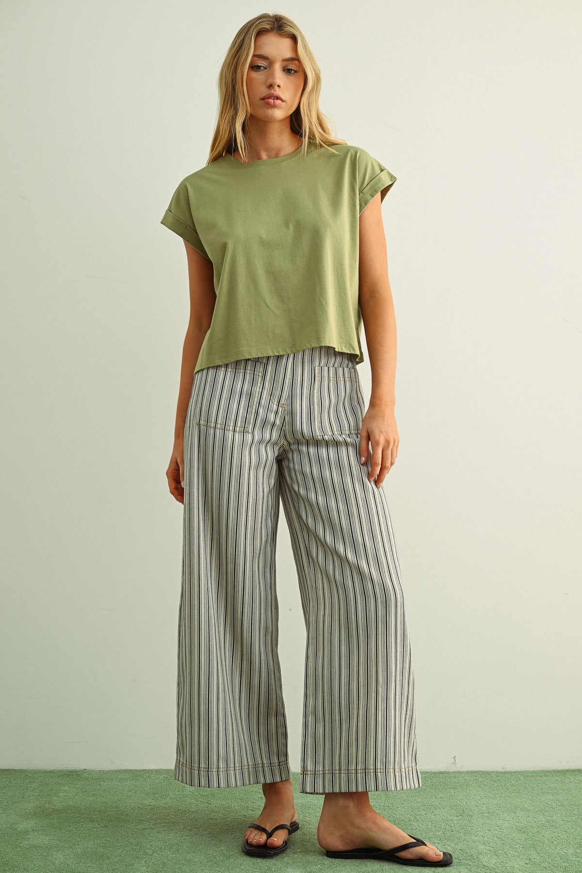 Woman wearing a green top and striped pants against a plain background
