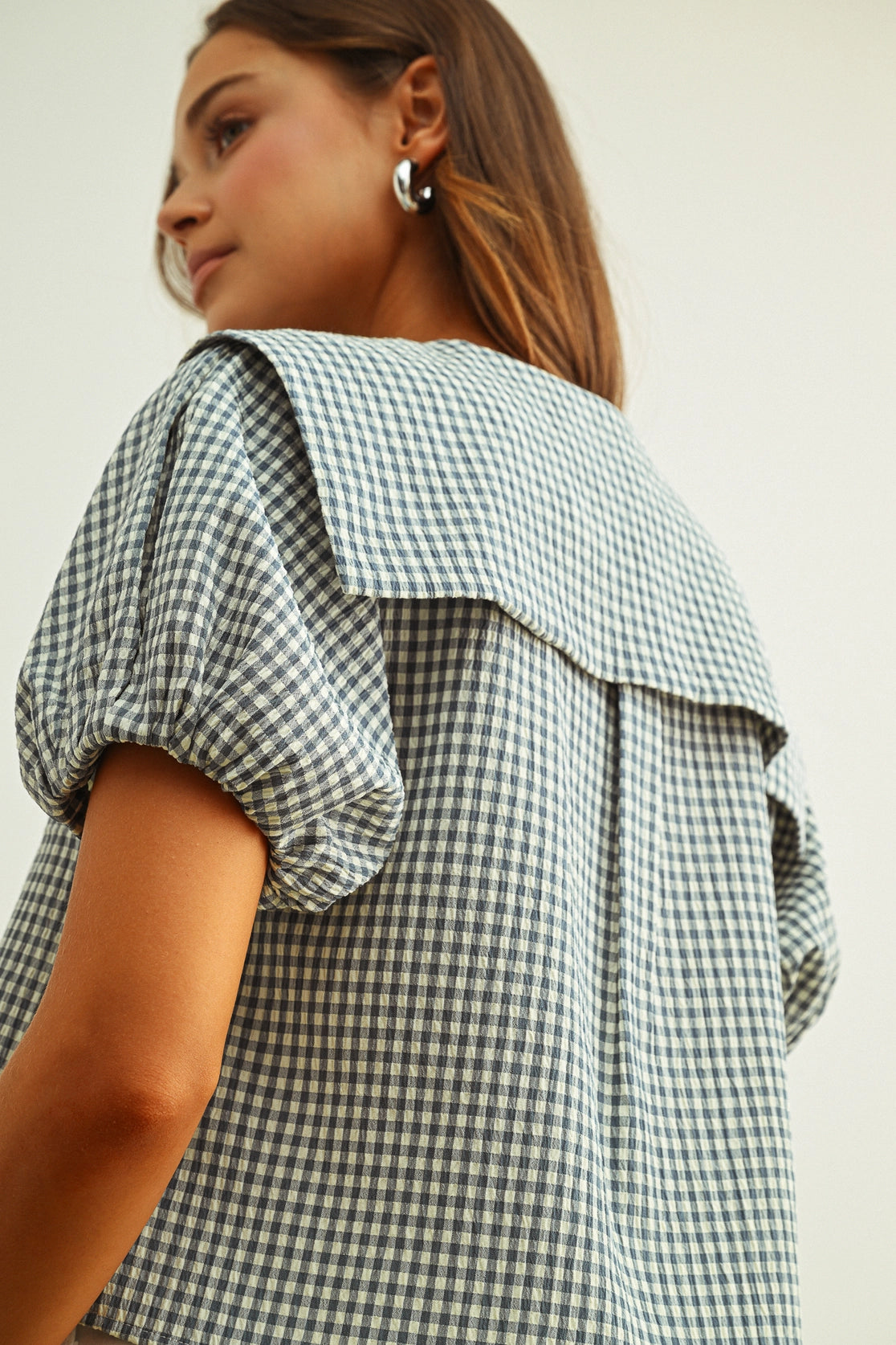 Woman wearing a green and white checkered blouse with puffed sleeves on a plain background