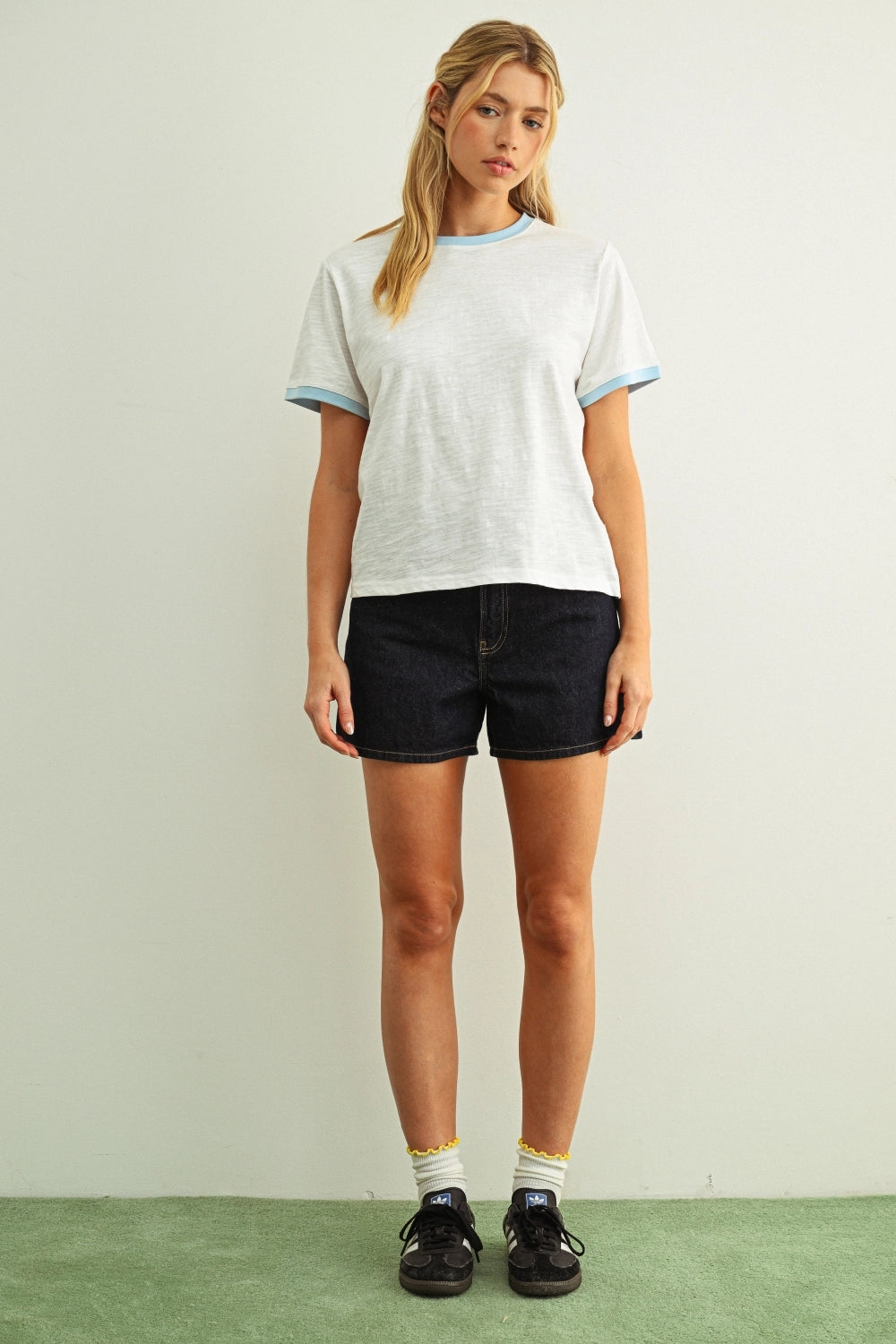 Woman modeling a white tee with a blue collar with black shorts against a white wall