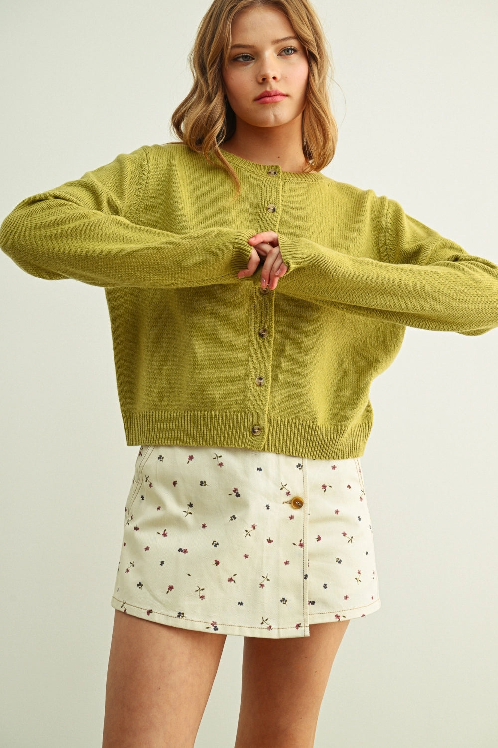 Woman wearing a green sweater and floral skirt on a plain background