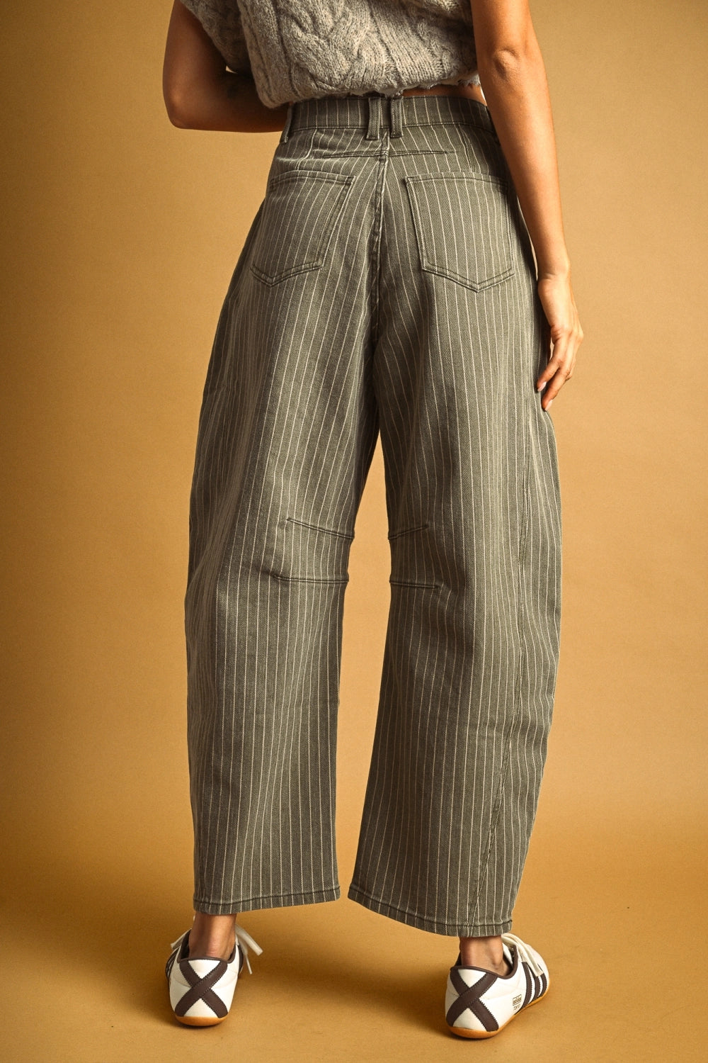 Woman wearing olive barrel jeans against a plain background.