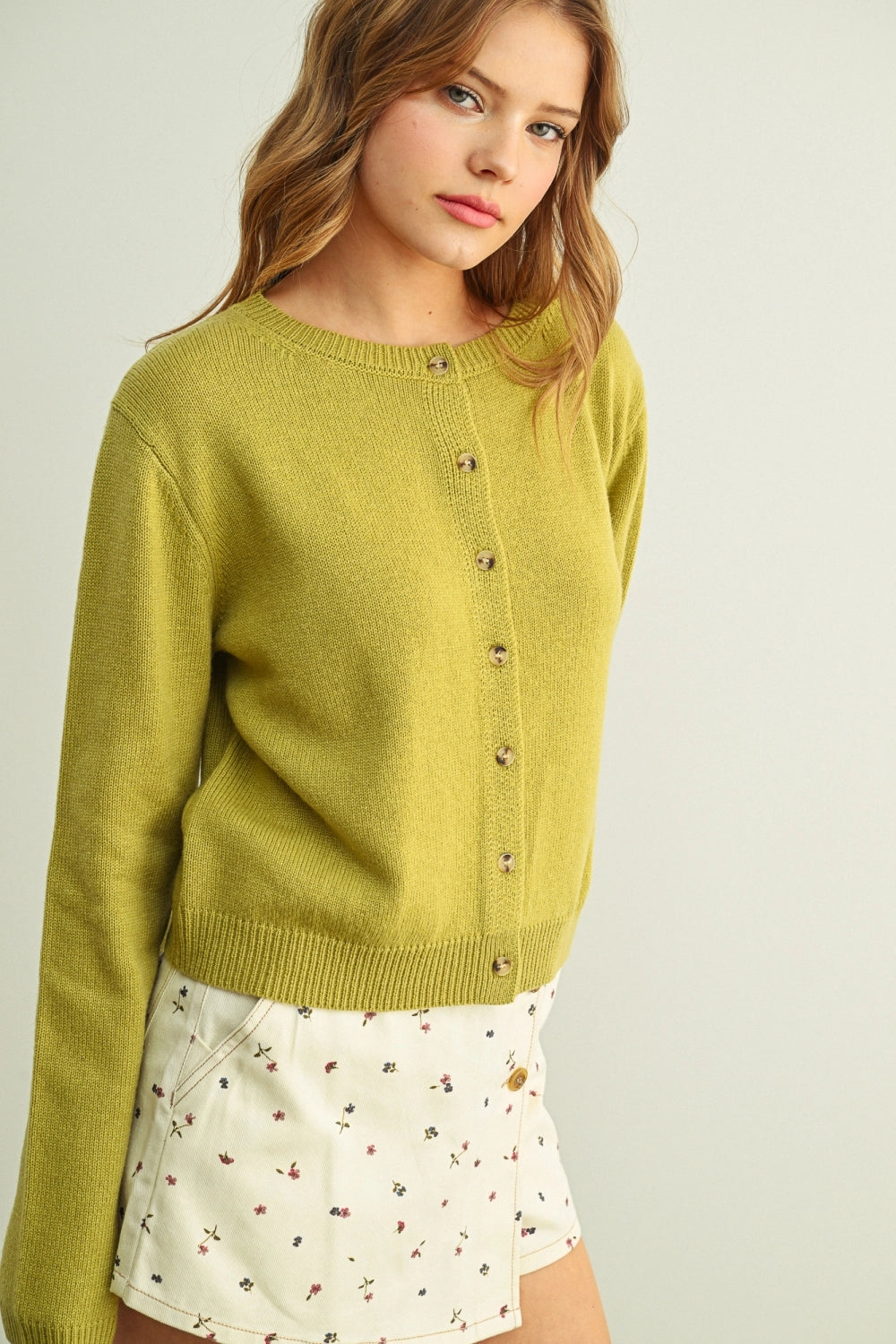 Woman wearing a green cardigan over a white floral dress on a plain background