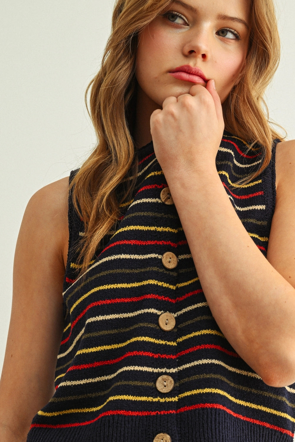 Woman wearing a sleeveless striped sweater with buttons on a plain background