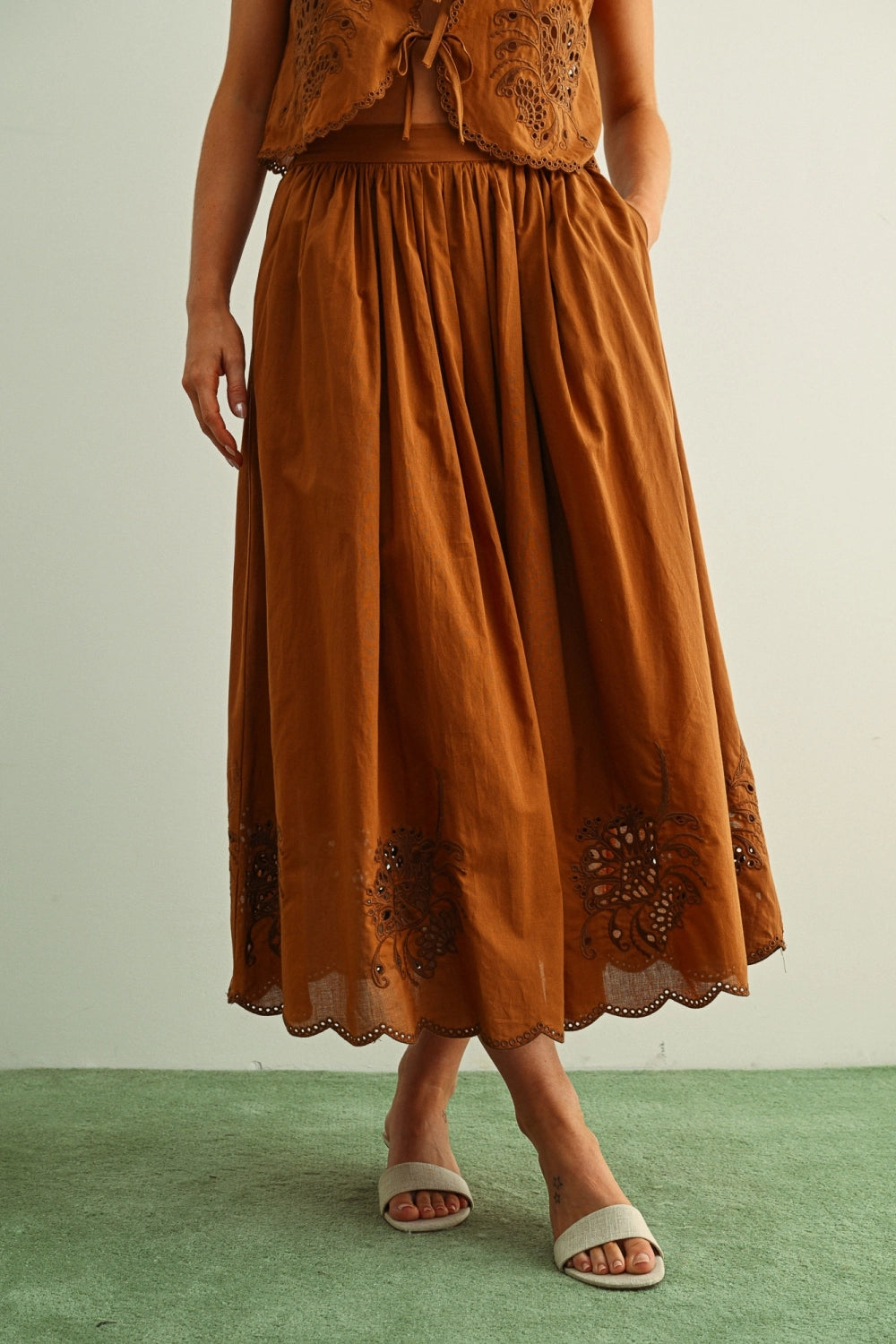 Woman wearing a brown dress with lace details on a green floor and light gray wall.