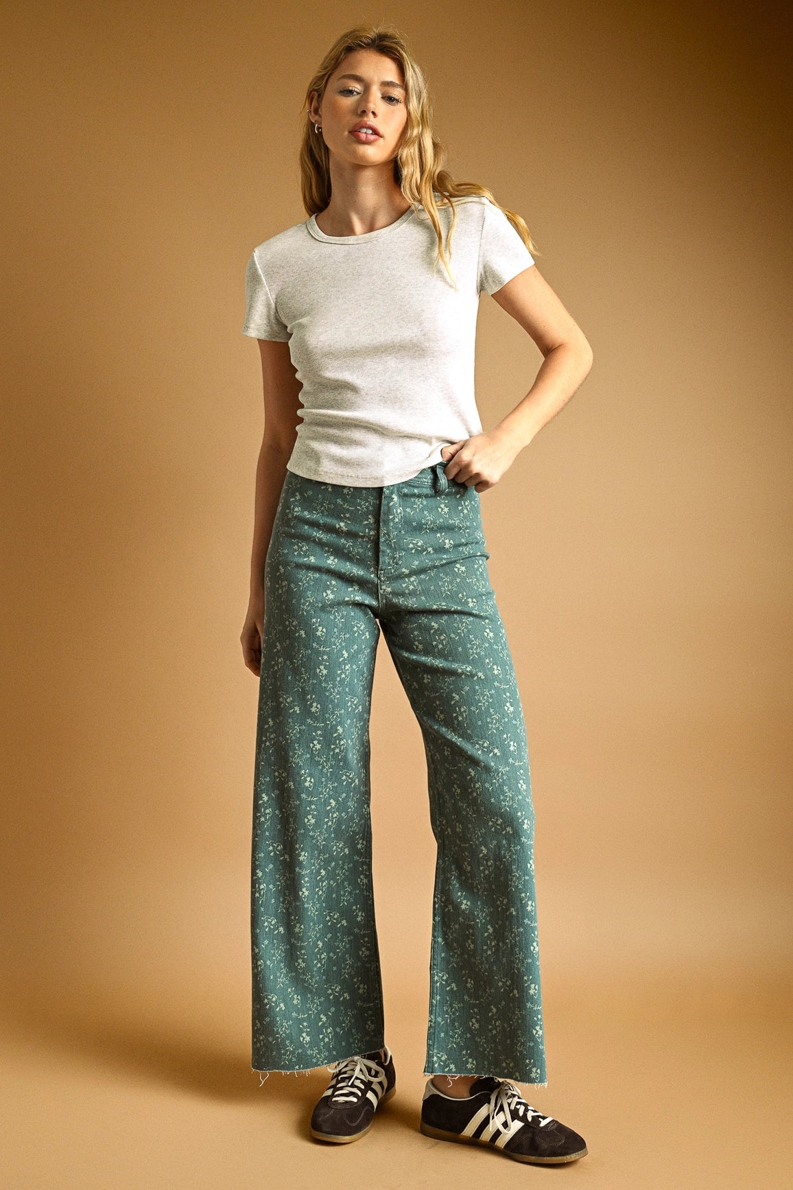 Woman wearing a white t-shirt and teal patterned pants on a beige background