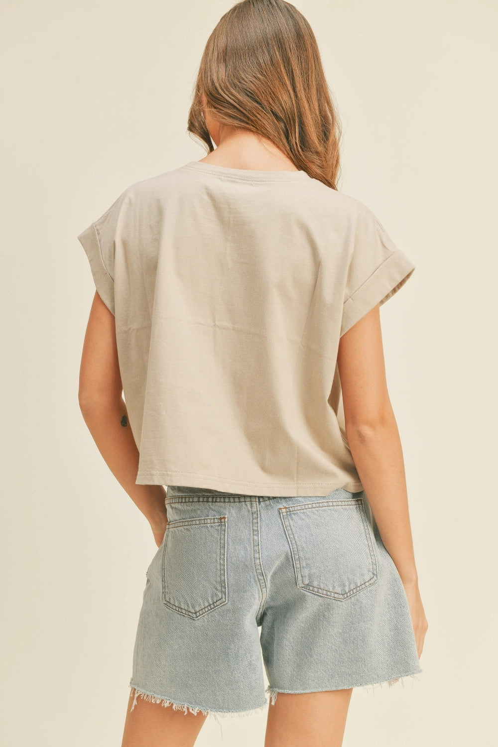 Person wearing a beige top and denim shorts on a plain background