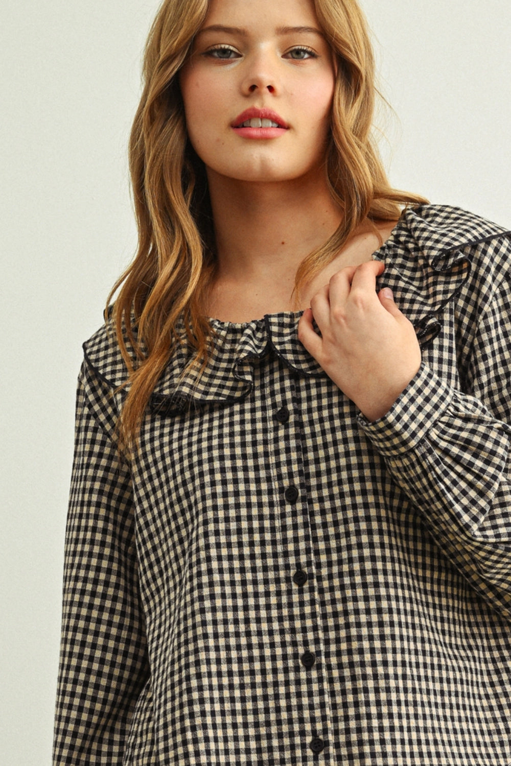 Woman wearing a black and white checkered blouse with a ruffled neckline.