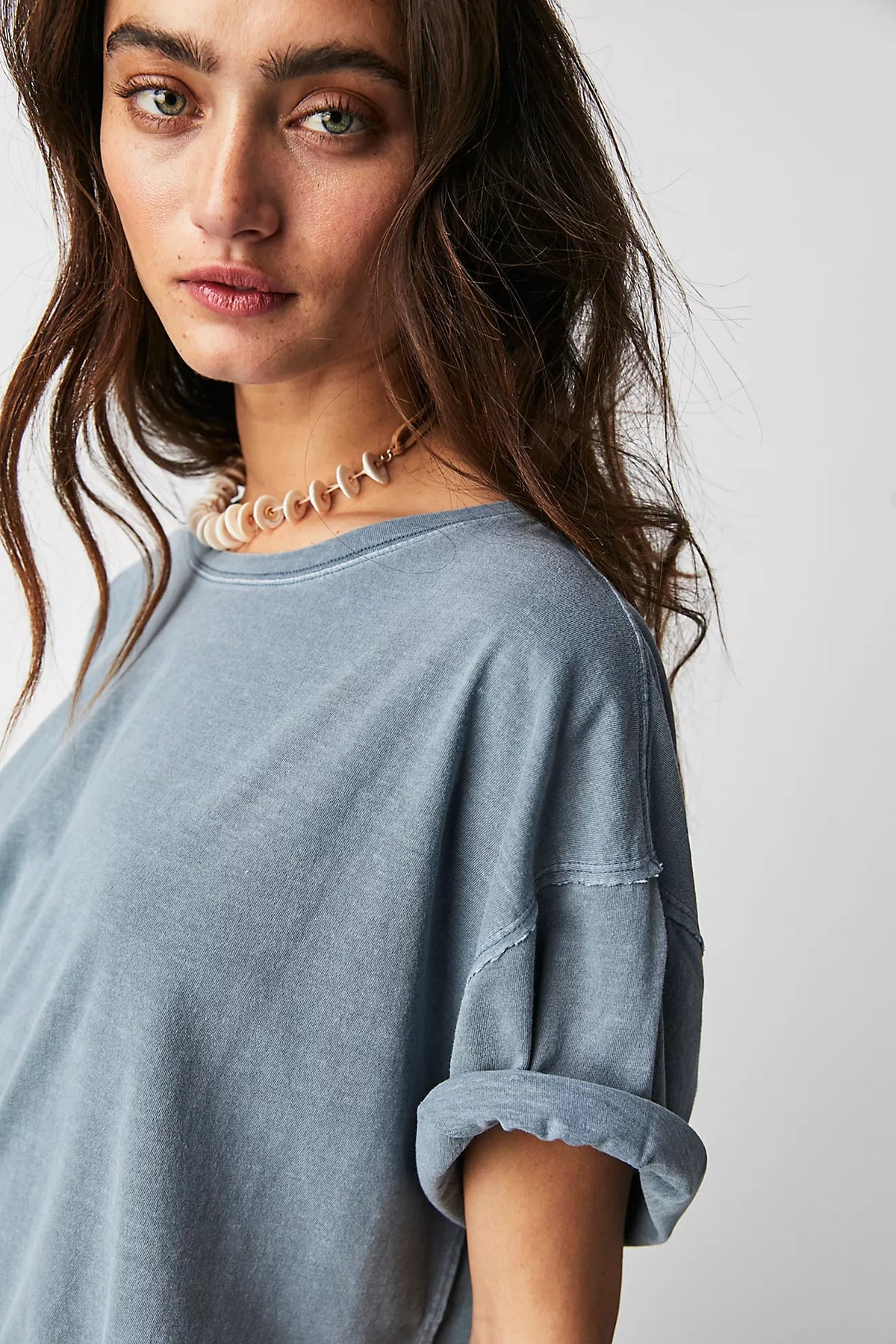 Woman wearing a light blue shirt with rolled-up sleeves against a plain background