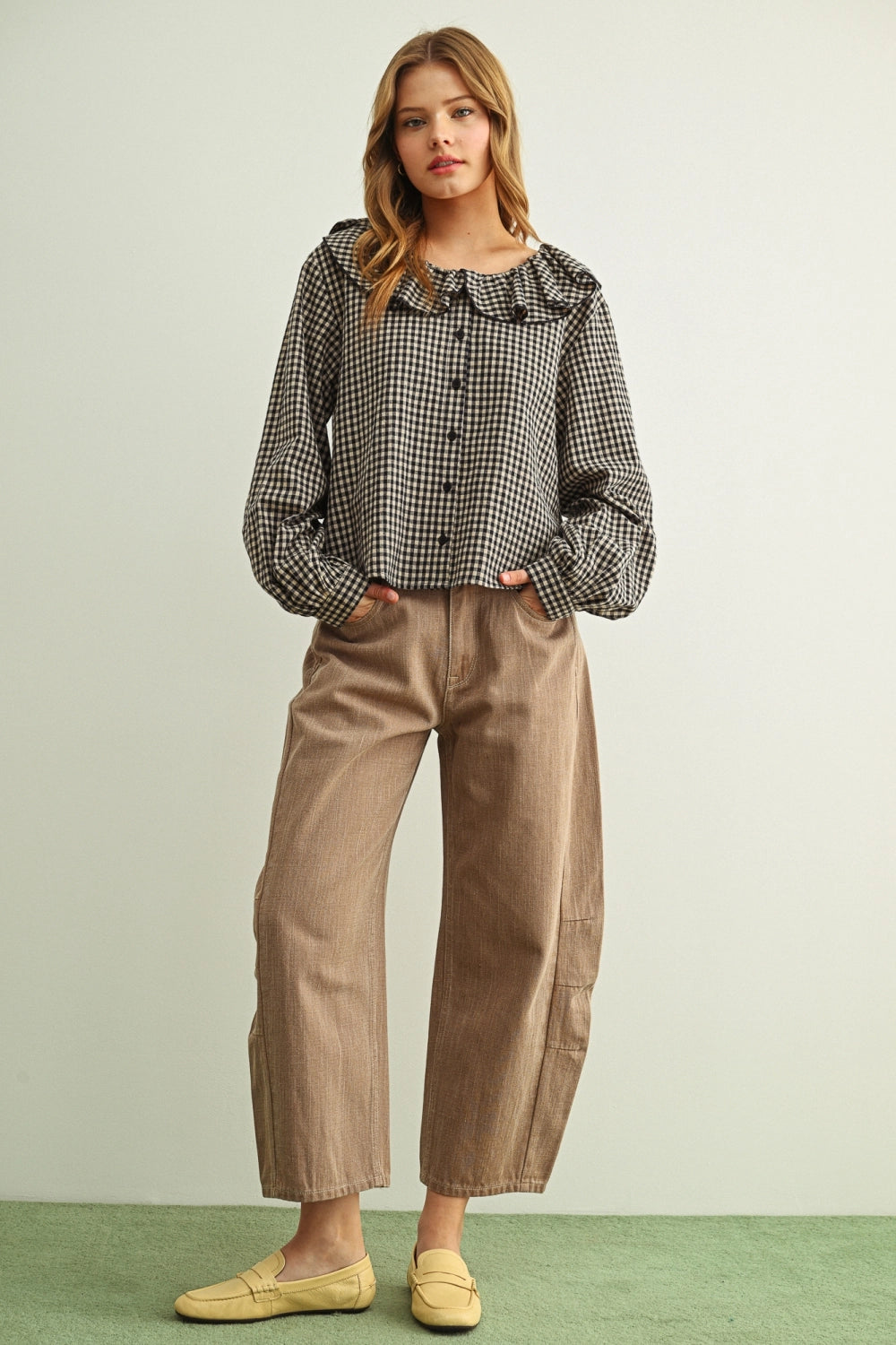 Woman wearing a checkered blouse and beige pants on a light green background