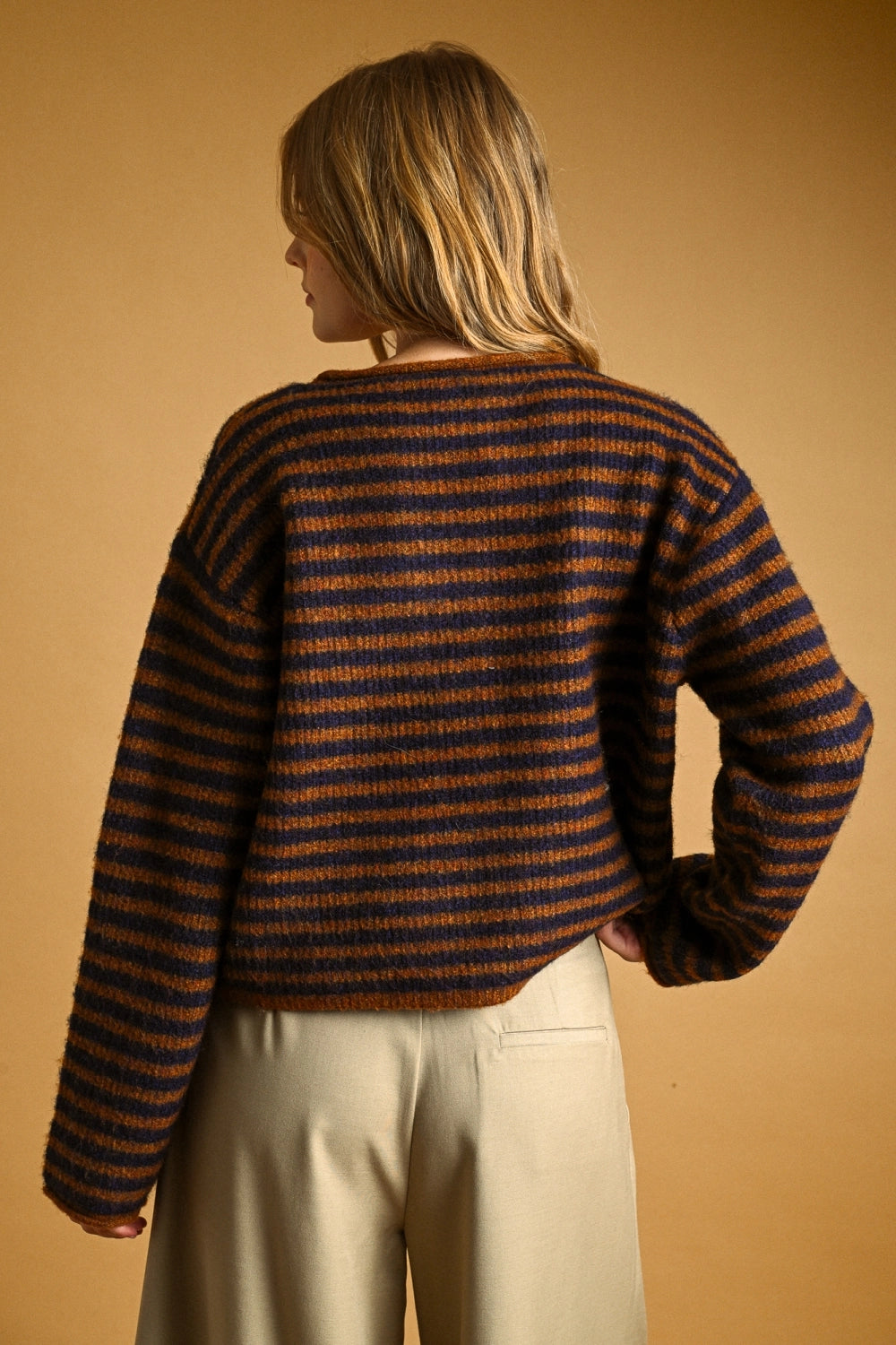 Person wearing a striped sweater and beige pants against a beige background
