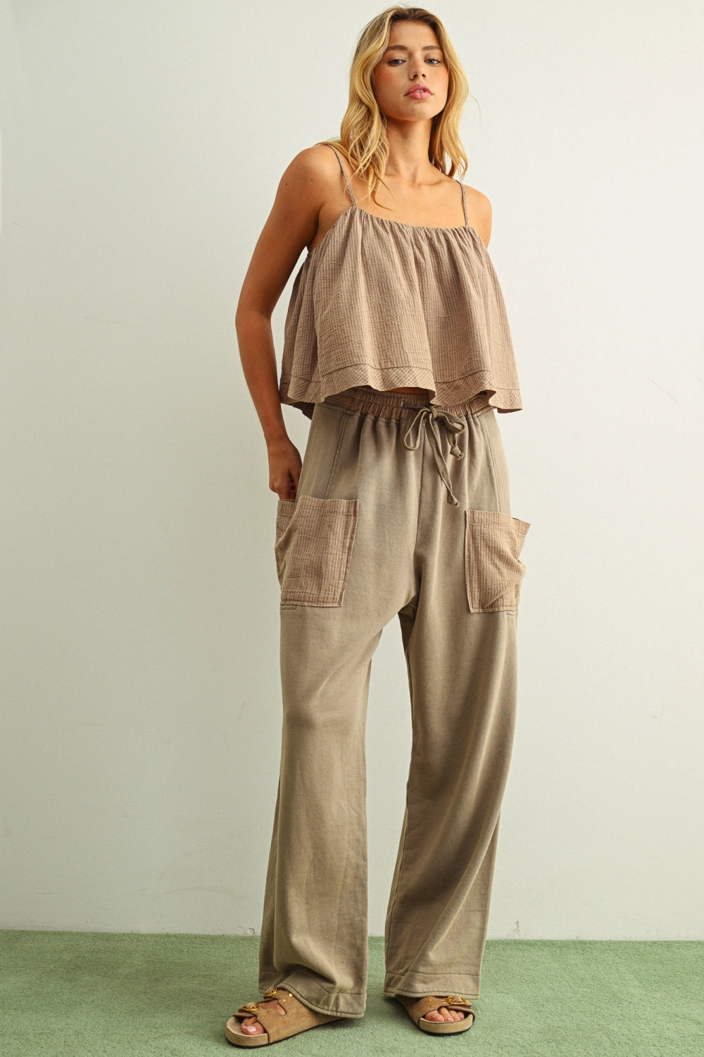 Woman wearing a beige top and pants against a plain background