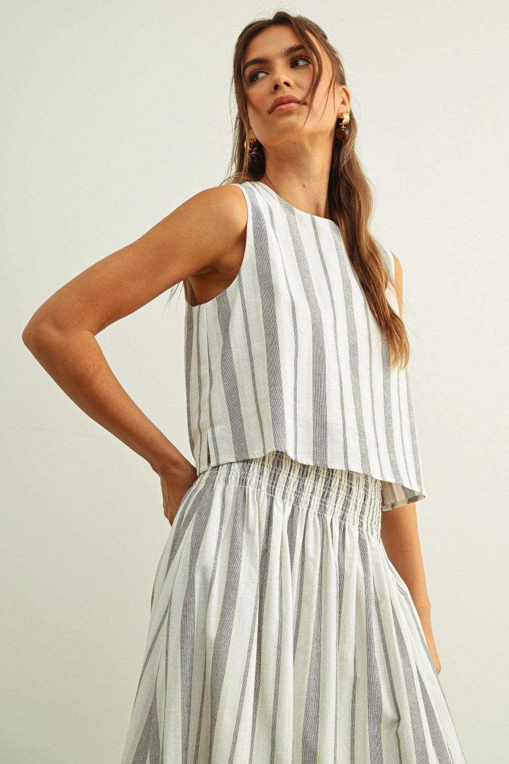 Woman wearing a sleeveless striped top and pants on a plain background