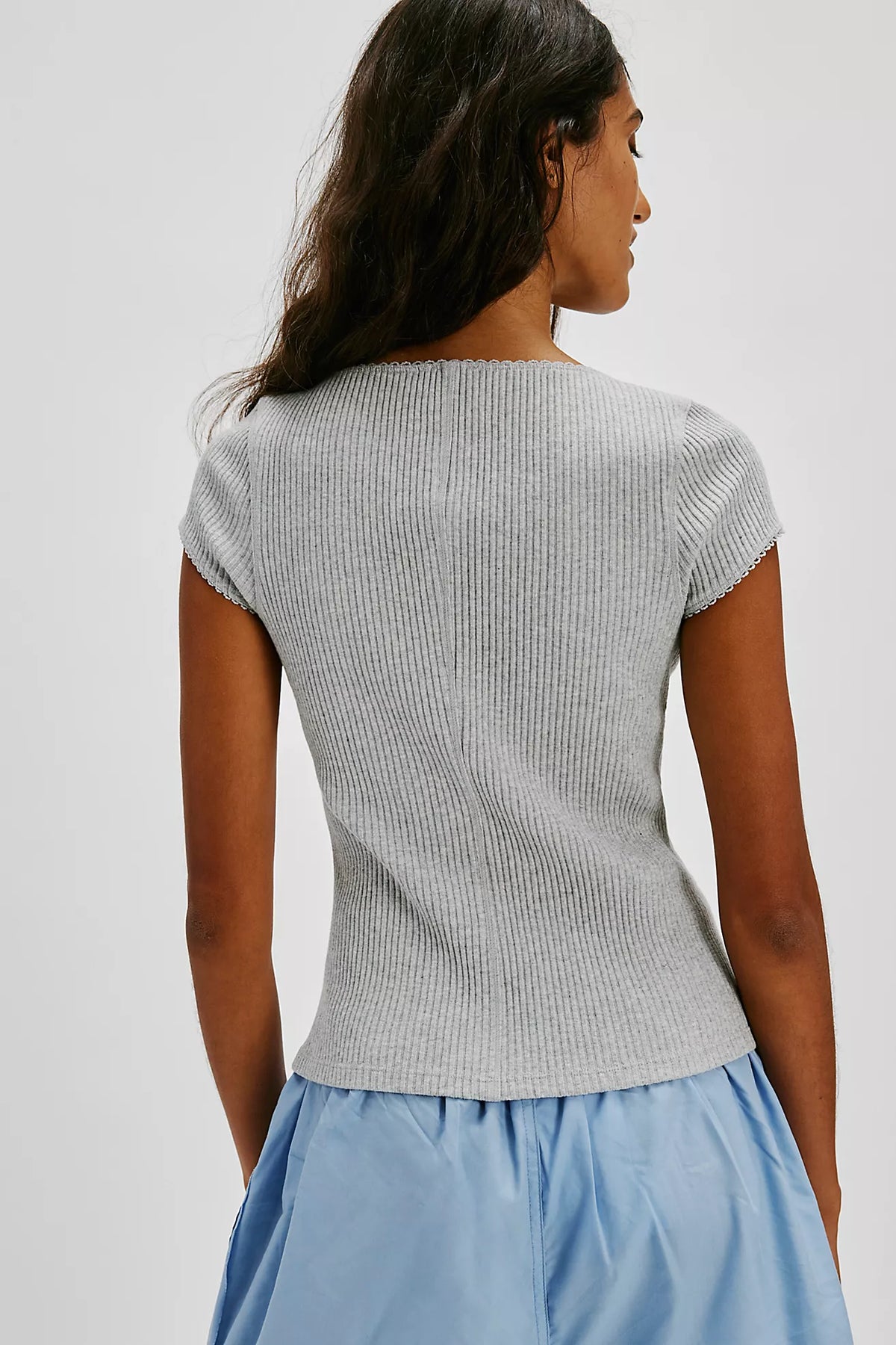 Woman wearing a gray ribbed sweater and light blue skirt on a plain background