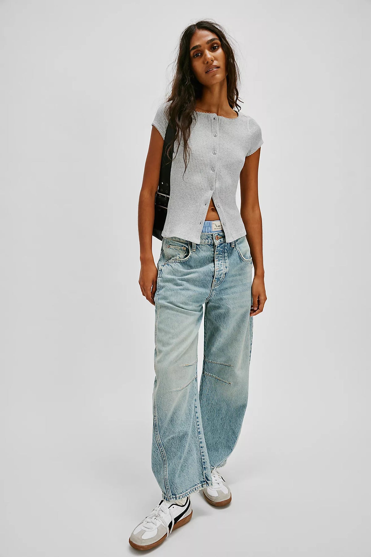 Woman wearing a light gray top and blue jeans on a white background