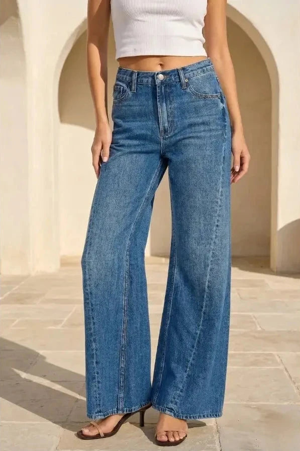 Person wearing blue wide-leg jeans and a white top in an outdoor setting.