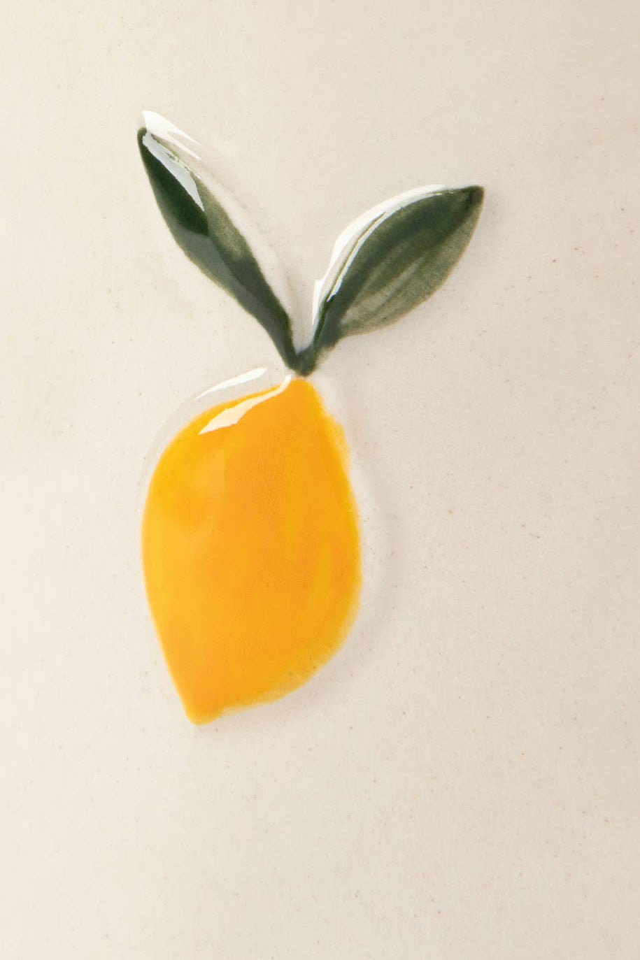 Yellow lemon-shaped object with green leaves on a beige background