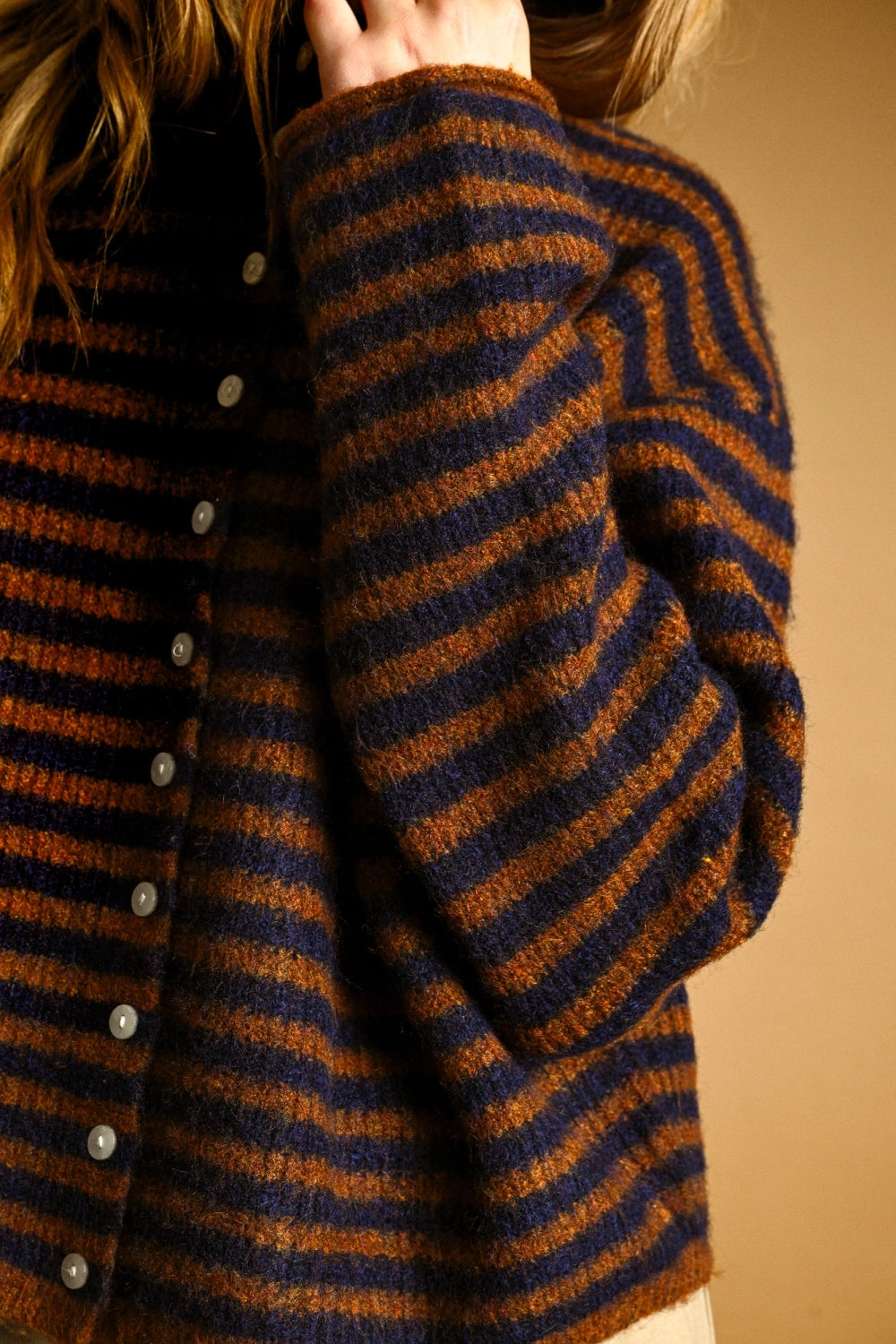 Close-up of a person wearing a striped sweater with brown and blue horizontal stripes on a beige background.