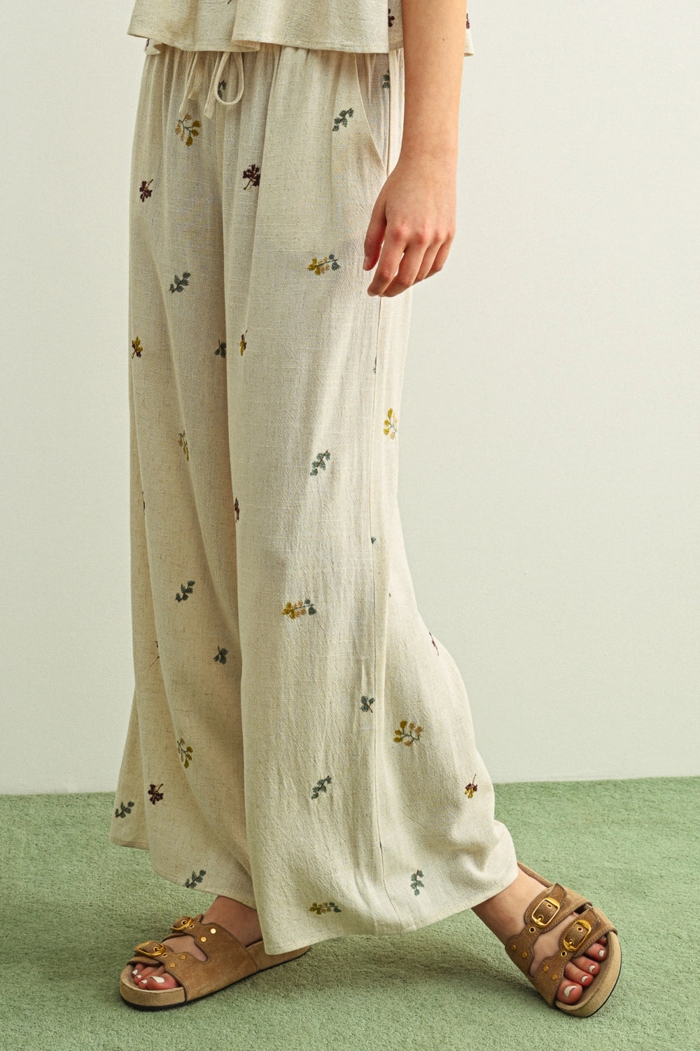 Person wearing light-colored pants with floral patterns and sandals on a green floor.