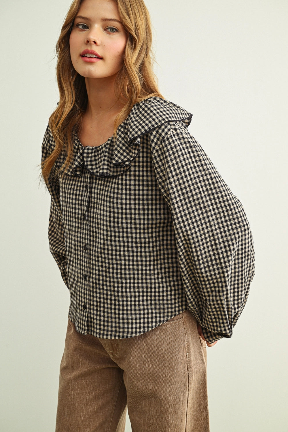 Woman wearing a black and white checkered blouse with ruffled details on a plain background