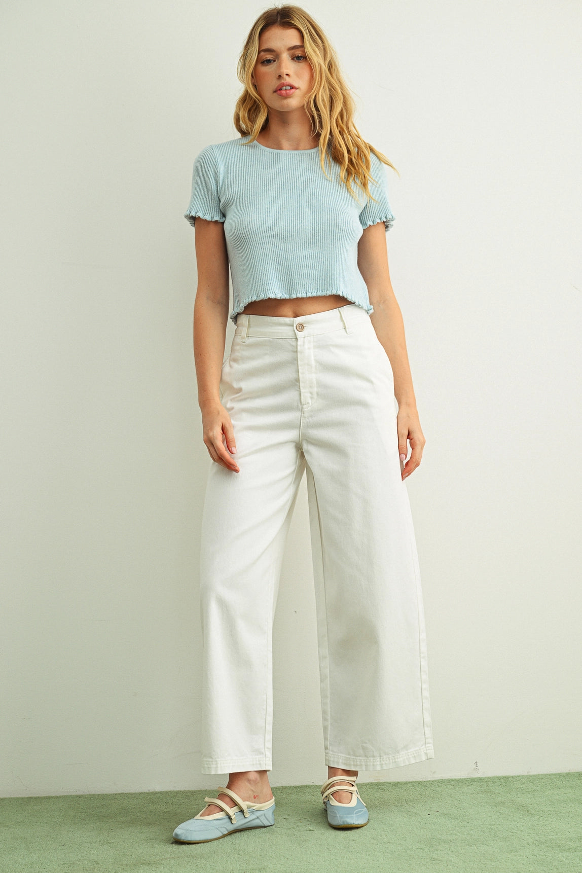 Woman wearing a light blue crop top and white pants against a plain background