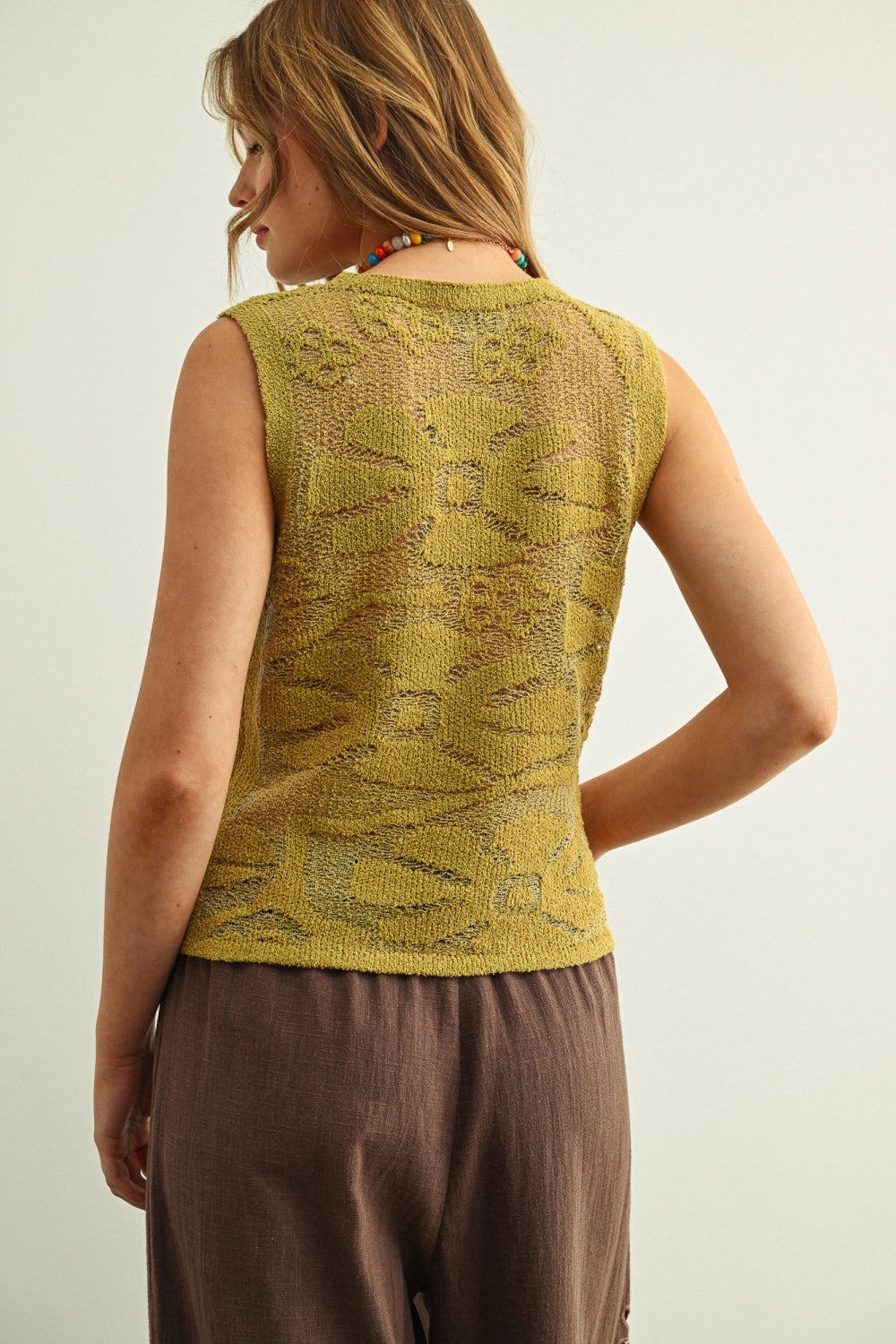 Woman wearing a green knitted vest against a plain background